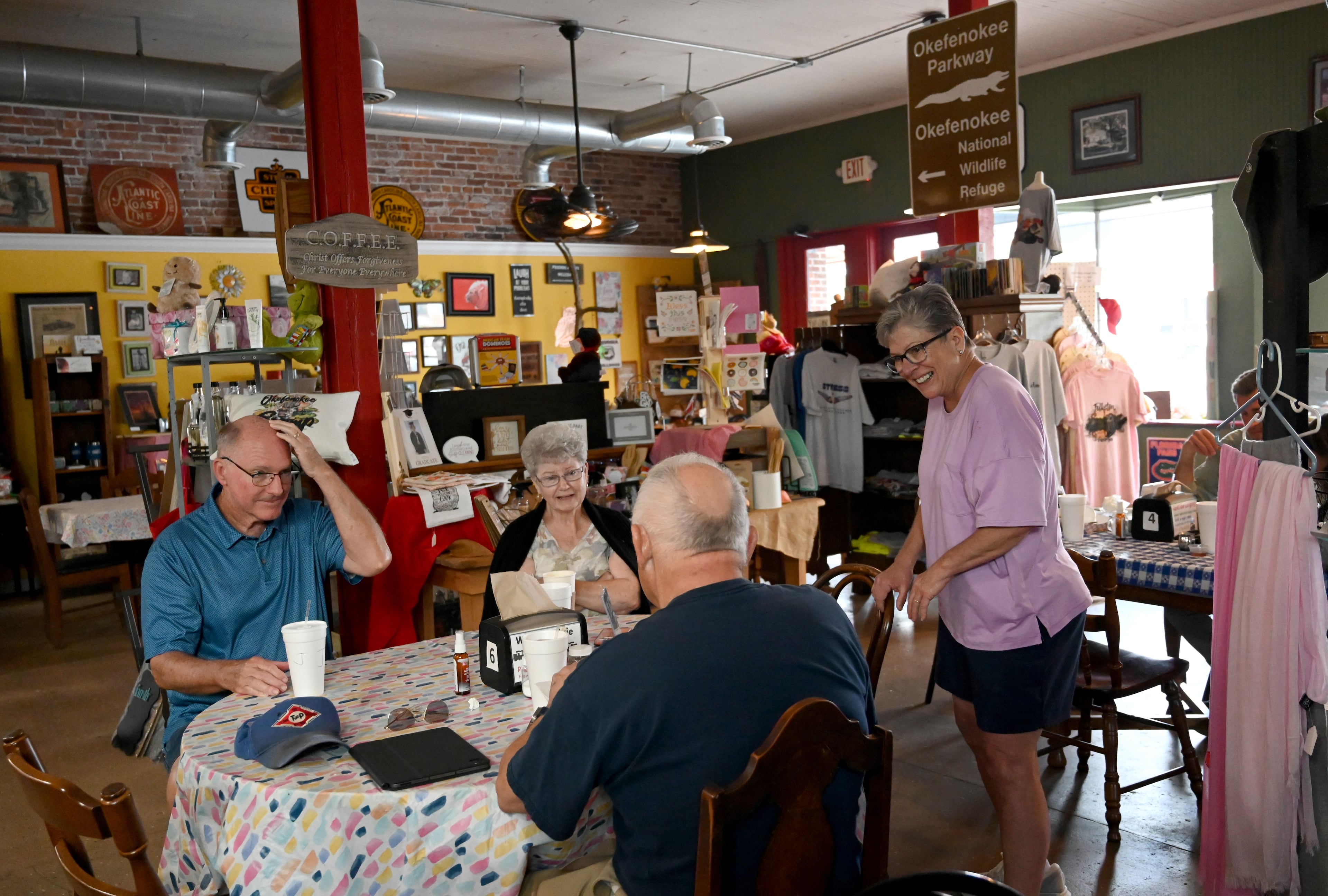 Dixie McGurn (right) talks with customers Barry Baines (foreground) and Linda Hannaford as her husband Jim McGurn (left) sits with the customers at Whistlin' Dixie Cafe on Tuesday, August 12, 2025, in Folkston. McGurn is a lifelong Folkston resident who believes a tourist economy built around the Okefenokee is a sustainable future for the area. (Hyosub Shin / AJC)