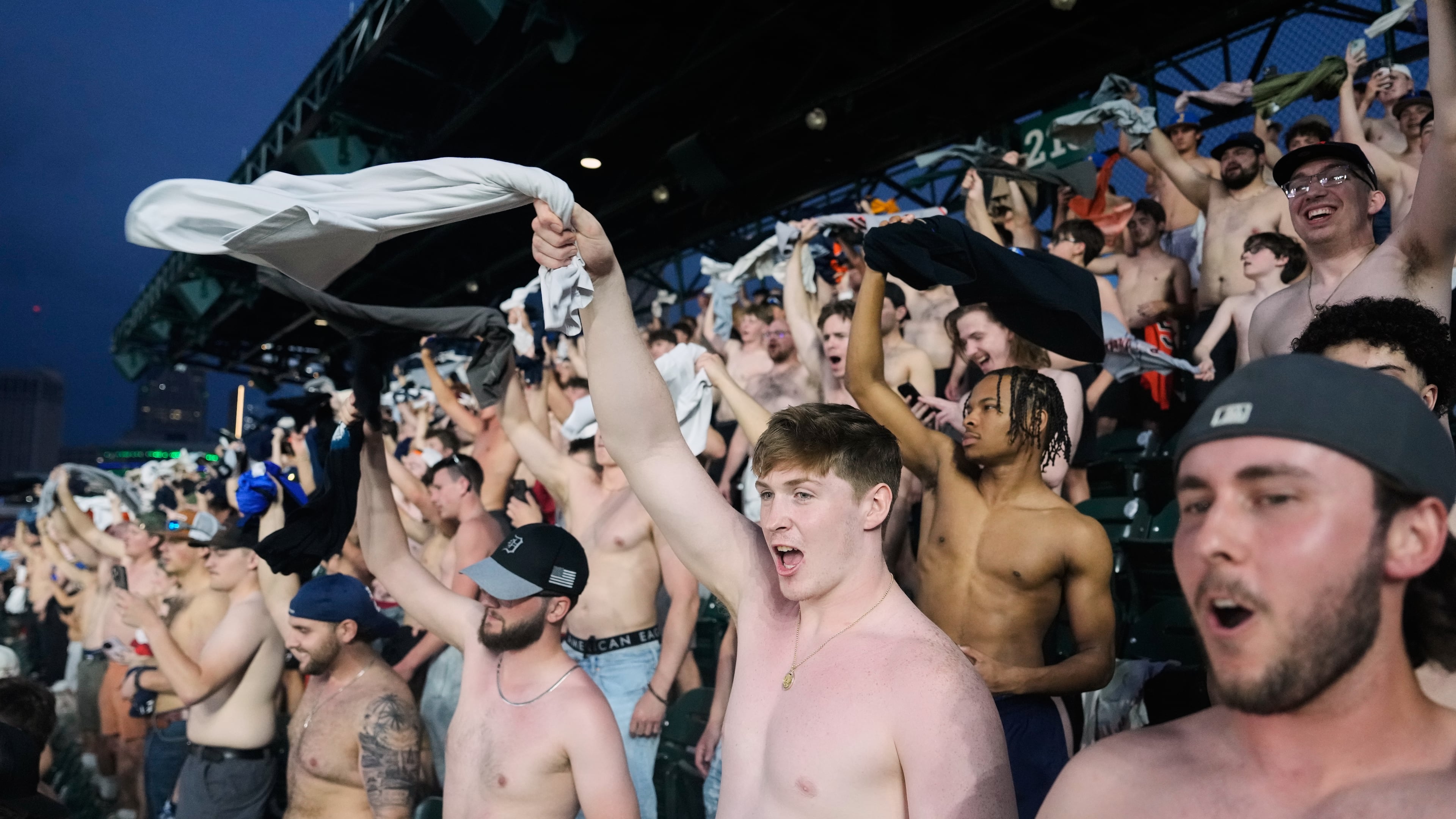 Fans cheer with their shirts off after heading to the upper deck outfield seating during the ninth inning of a baseball game between the Detroit Tigers and Cleveland Guardians Tuesday, May 19, 2026, in Detroit. (AP Photo/Paul Sancya)