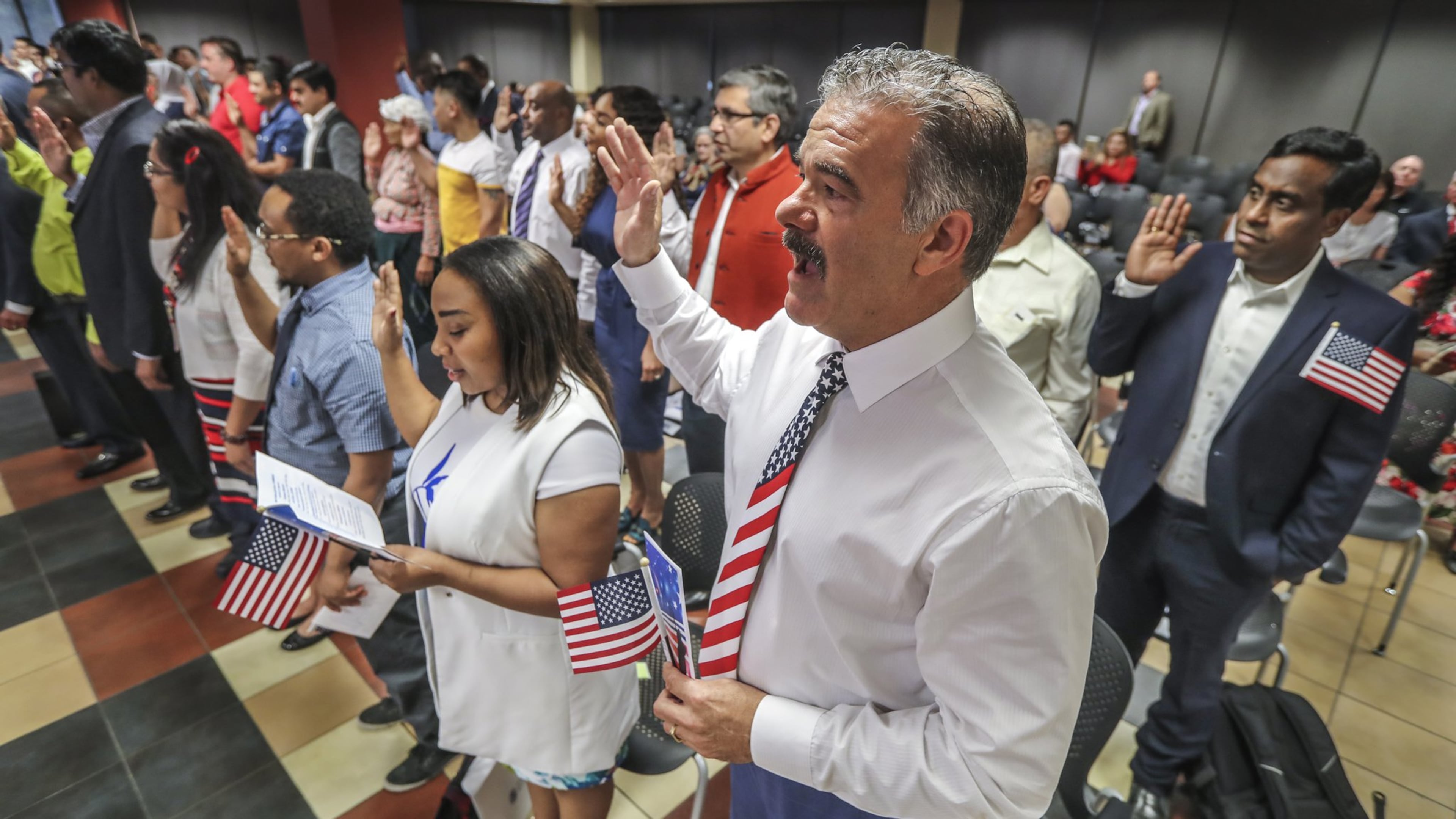 Florence Preston from Kenya, Jerry Fjerstad from the United Kingdom and Naveen Diddige from India raise their hands as the USCIS Atlanta district director administers the oath of allegiance to new citizens on July 3, 2019. (John Spink/AJC)