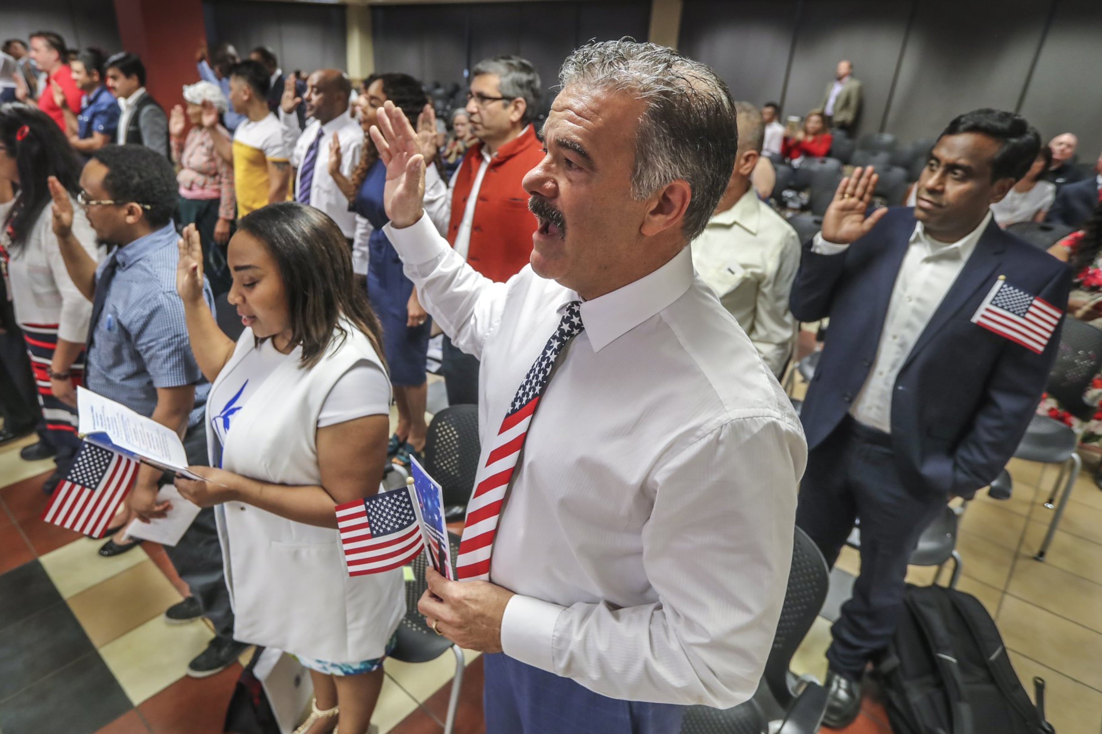 Florence Preston from Kenya, Jerry Fjerstad from the United Kingdom and Naveen Diddige from India raise their hands as the USCIS Atlanta district director administers the oath of allegiance to new citizens on July 3, 2019. (John Spink/AJC)