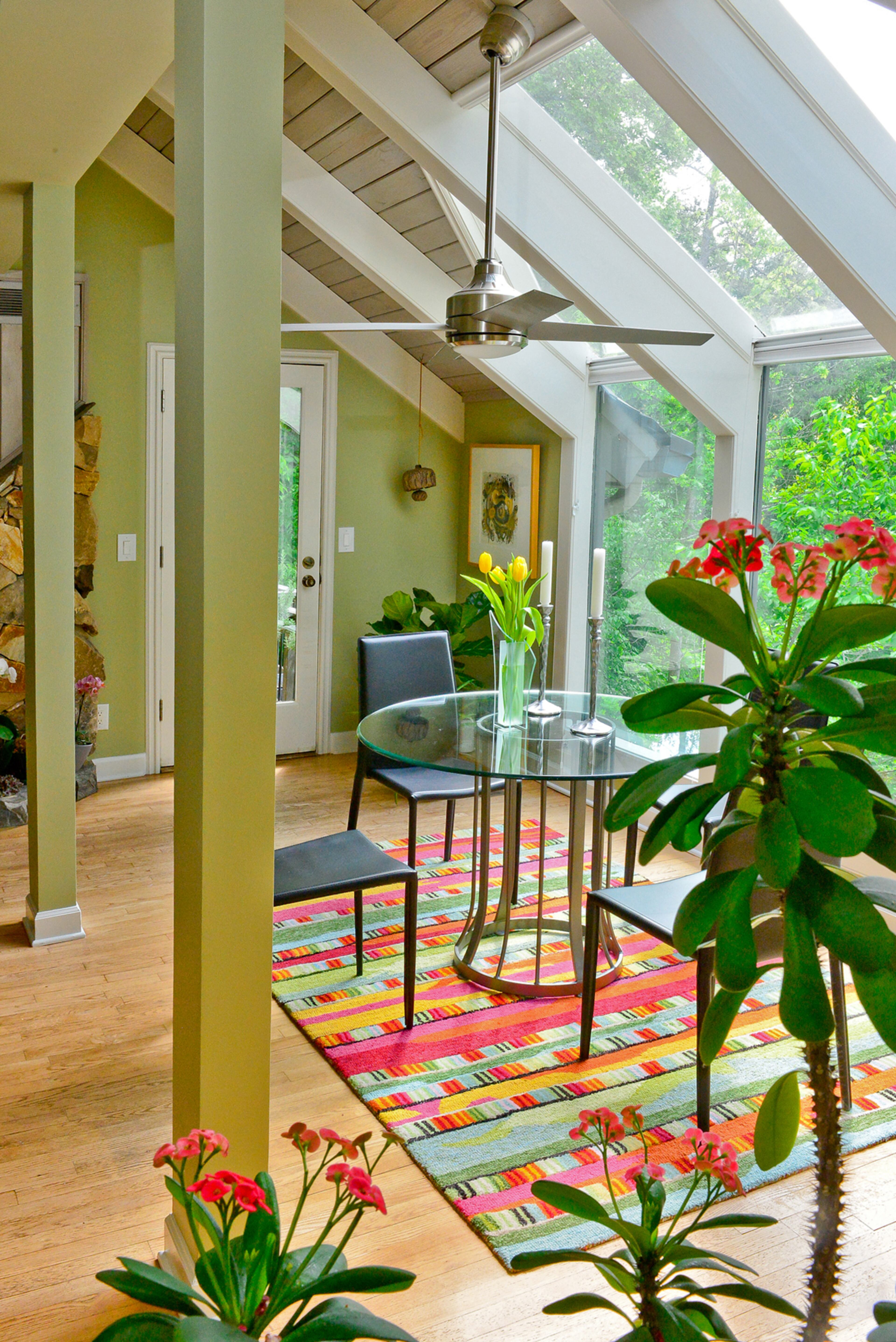 Eye-catching blooms match the colorful rug from Havertys in this breakfast room with a treetop view. Modern chairs from Modani and glass skylights and windows are juxtaposed with the rustic tongue-and-groove stained wooden ceiling and painted white beams.