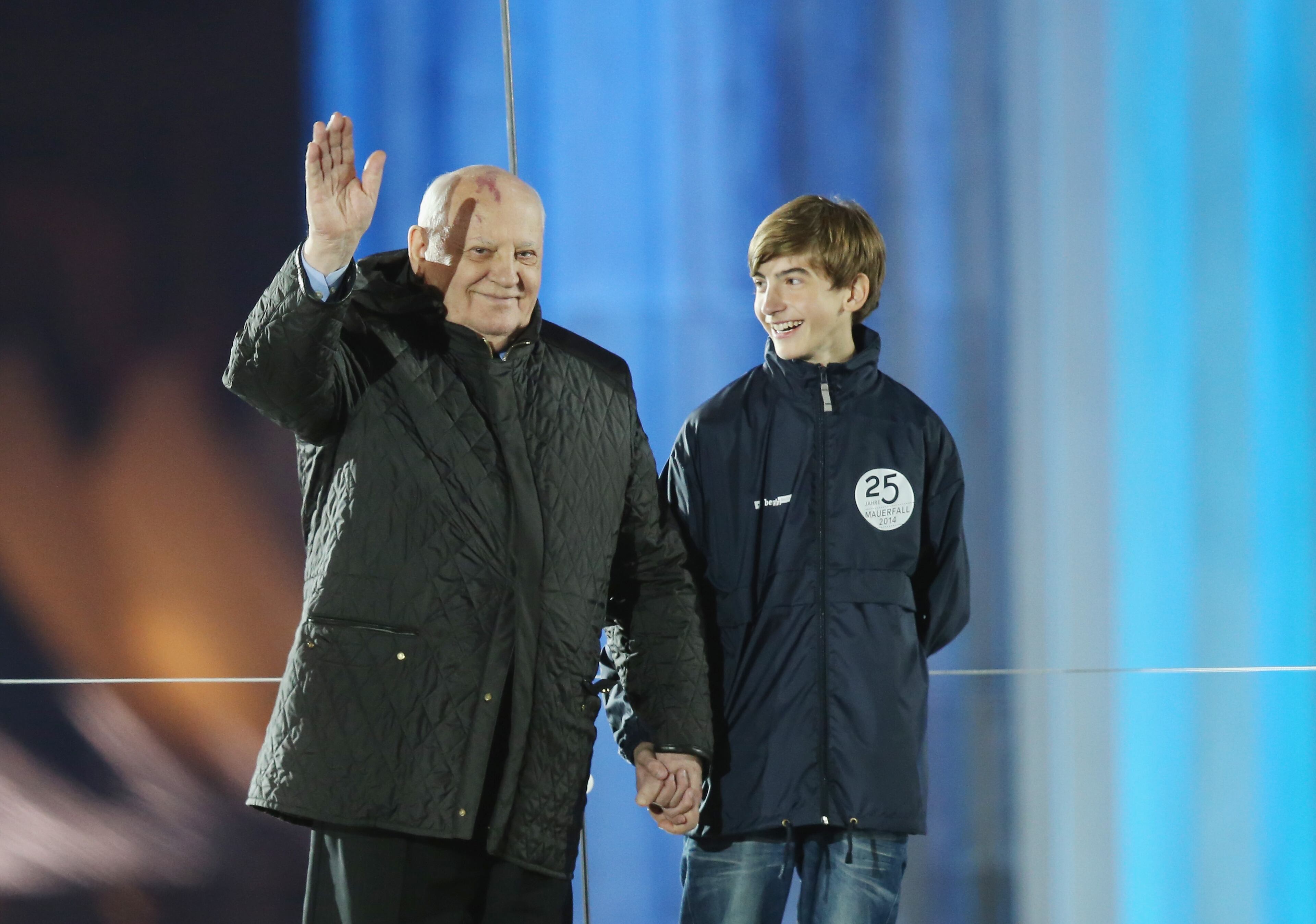 Former Soviet leader Mikhail Gorbachev waves at the Brandenburg Gate during celebrations on the 25th anniversary of the fall of the Berlin Wall on November 9, 2014 in Berlin, Germany. The city of Berlin is commemorating the 25th anniversary of the fall of the Berlin Wall with an installation of 6,800 lamps coupled with illuminated balloons along a 15km route where the Wall once ran and divided the city into capitalist West and communist East. The fall of the Wall on November 9, 1989, was among the most powerful symbols of the revolutions that swept through the communist countries of Eastern Europe and heralded the end of the Cold War. Built by the communist authorities of East Germany in 1961, the Wall prevented East Germans from fleeing west and was equipped with guard towers and deadly traps. (Photo by Sean Gallup/Getty Images)