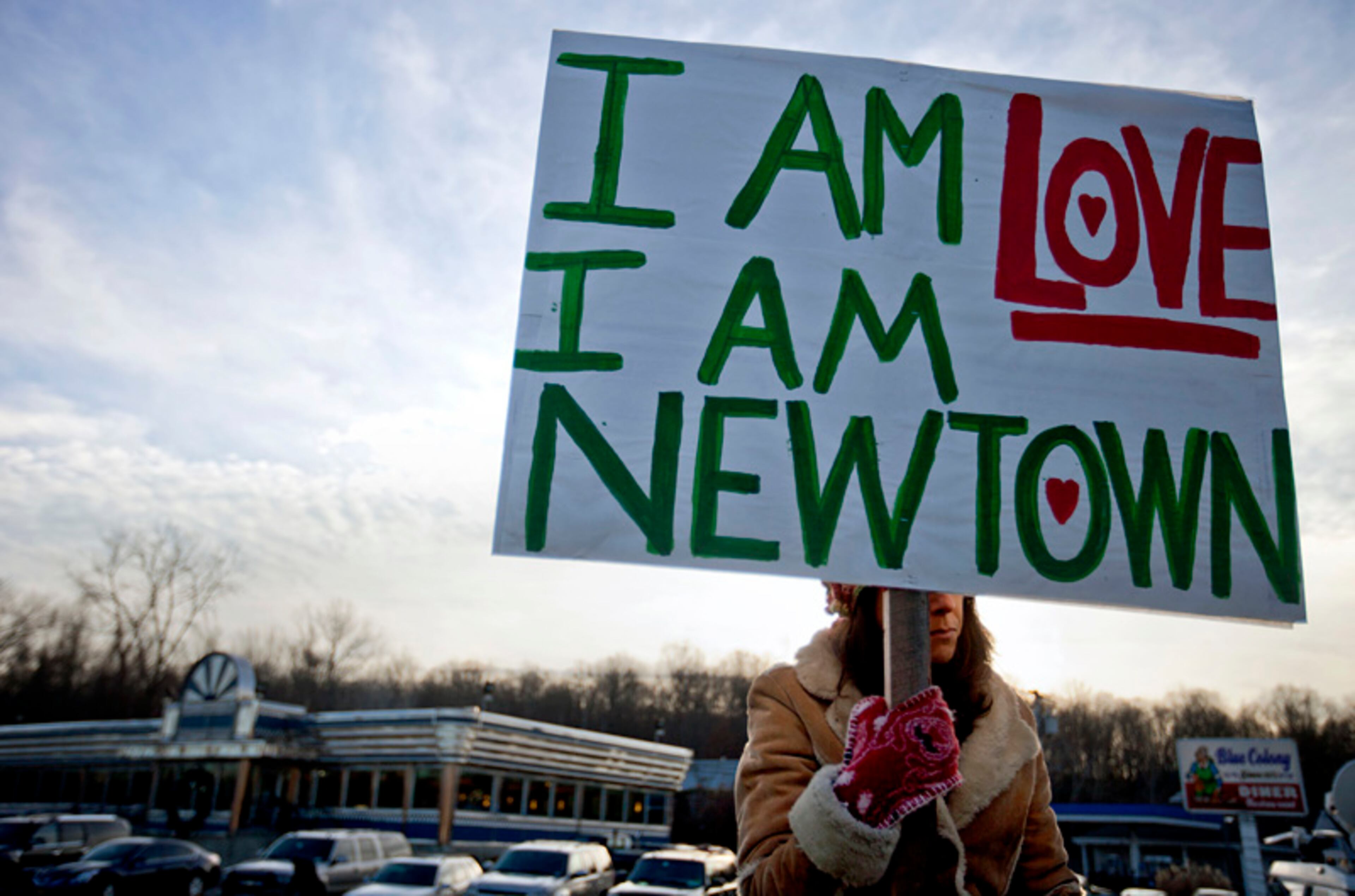A Newtown, Conn., resident, who declined to give her name, sits at an intersection holding a sign for passing motorists up the road from the Sandy Hook Elementary School, Saturday, Dec. 15, 2012, in Newtown, Conn.