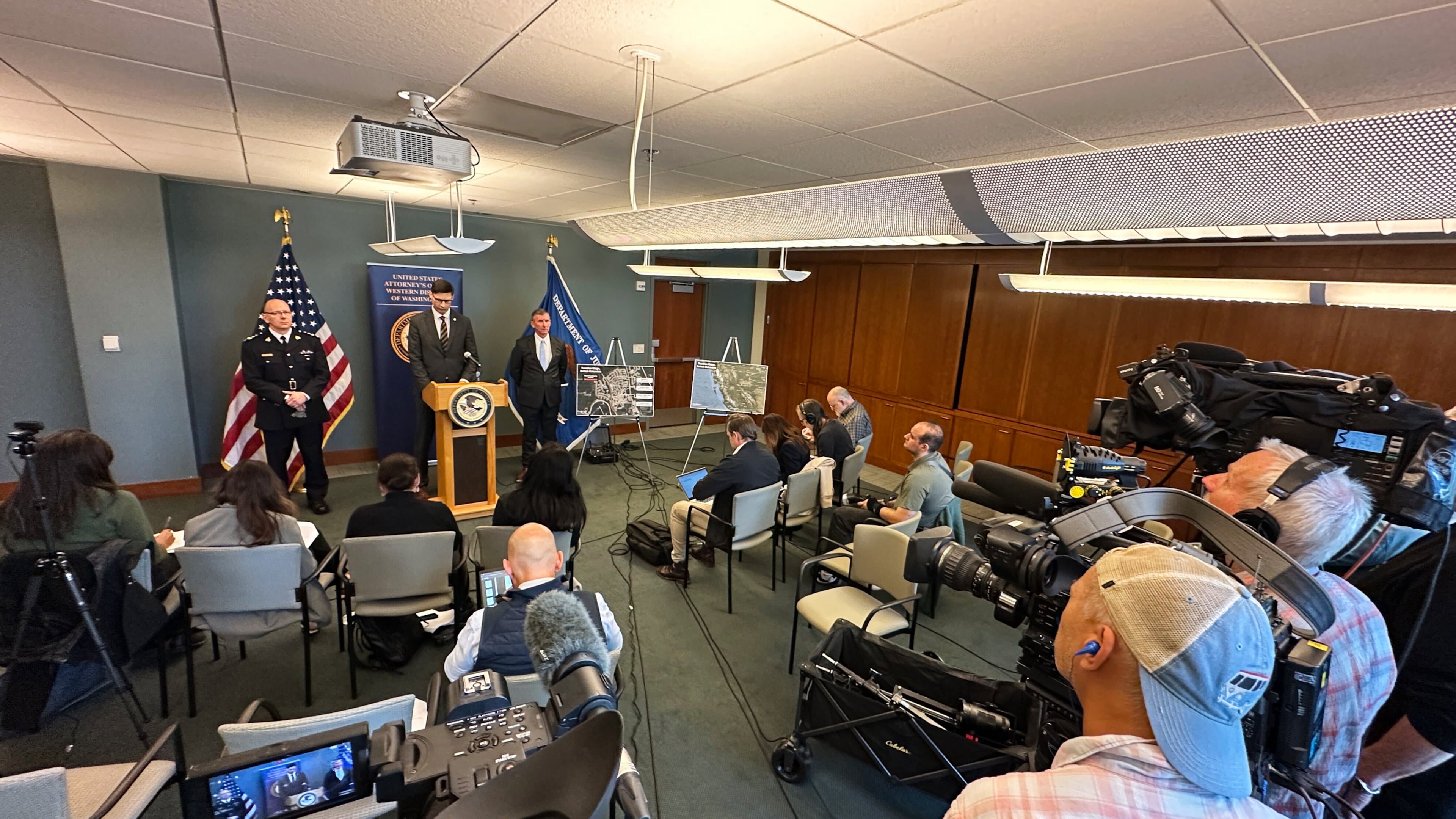 In this photo taken with a smartphone, Mike Herrington, the FBI special agent in charge, speaks to the media on Tuesday, Oct. 6, 2026, in Seattle. Standing next to Herrington are Elija Rain, the assistant commissioner of the British Columbia Royal Canadian Mounted Police, left, and Acting U.S. Attorney Neil Floyd, right. (AP Photo/Manuel Valdes)