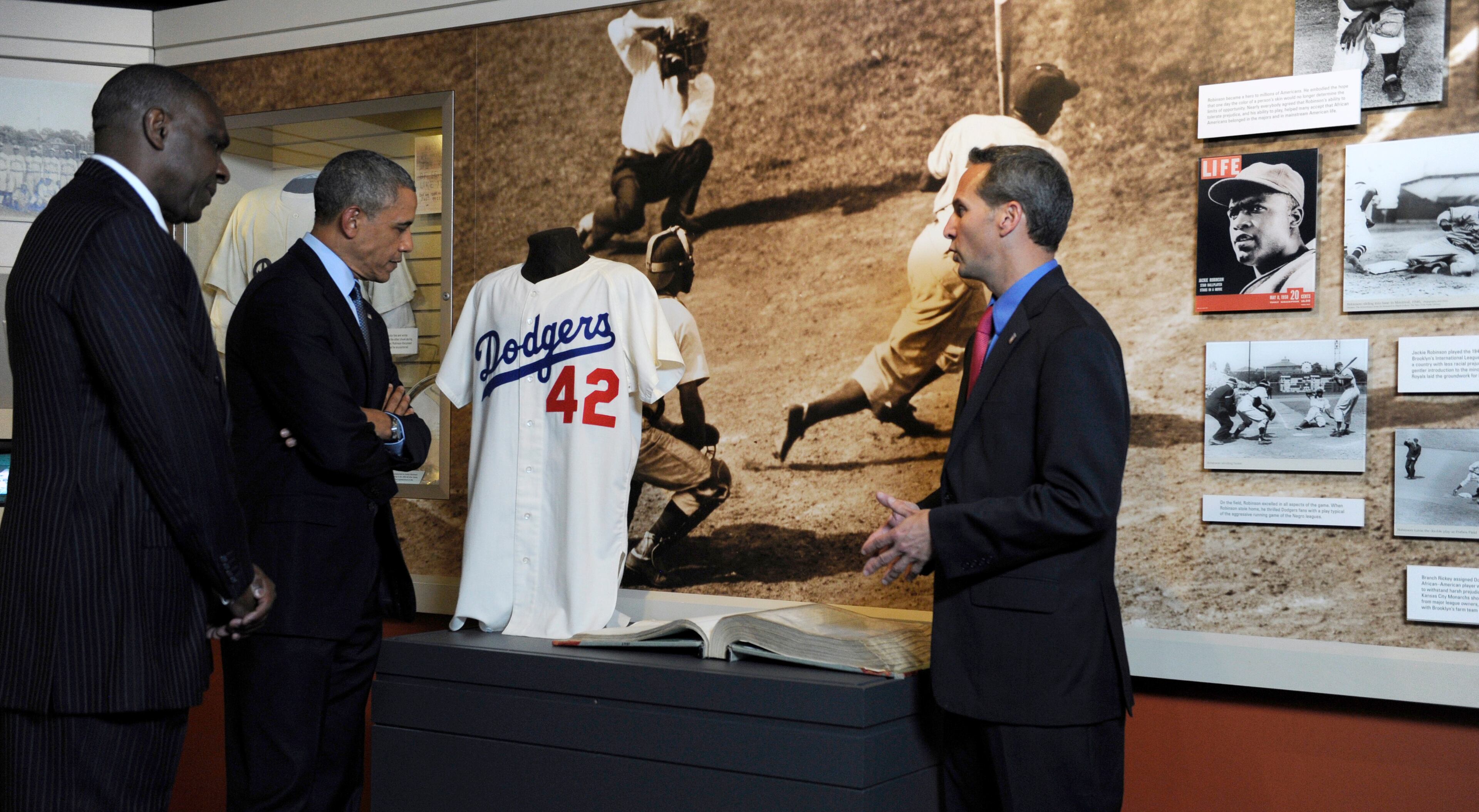President Barack Obama, accompanied by Baseball Hall of Fame President Jeff Idelson, right, and baseball hall of fame member Andre Dawson, inducted in 2010, looks over a collection item from Jackie Robinson during a tour the Baseball Hall of Fame in Cooperstown, N.Y., Thursday, May 22, 2014. Obama visited the museum to highlight tourism and steps to help spur international visits to the 50 states. Obama said the overall U.S. economy and local businesses will benefit if it isn't a hassle for people from other countries to visit the U.S. and spend money at its hotels, restaurants, tourist destinations and other businesses. (AP Photo/Susan Walsh)