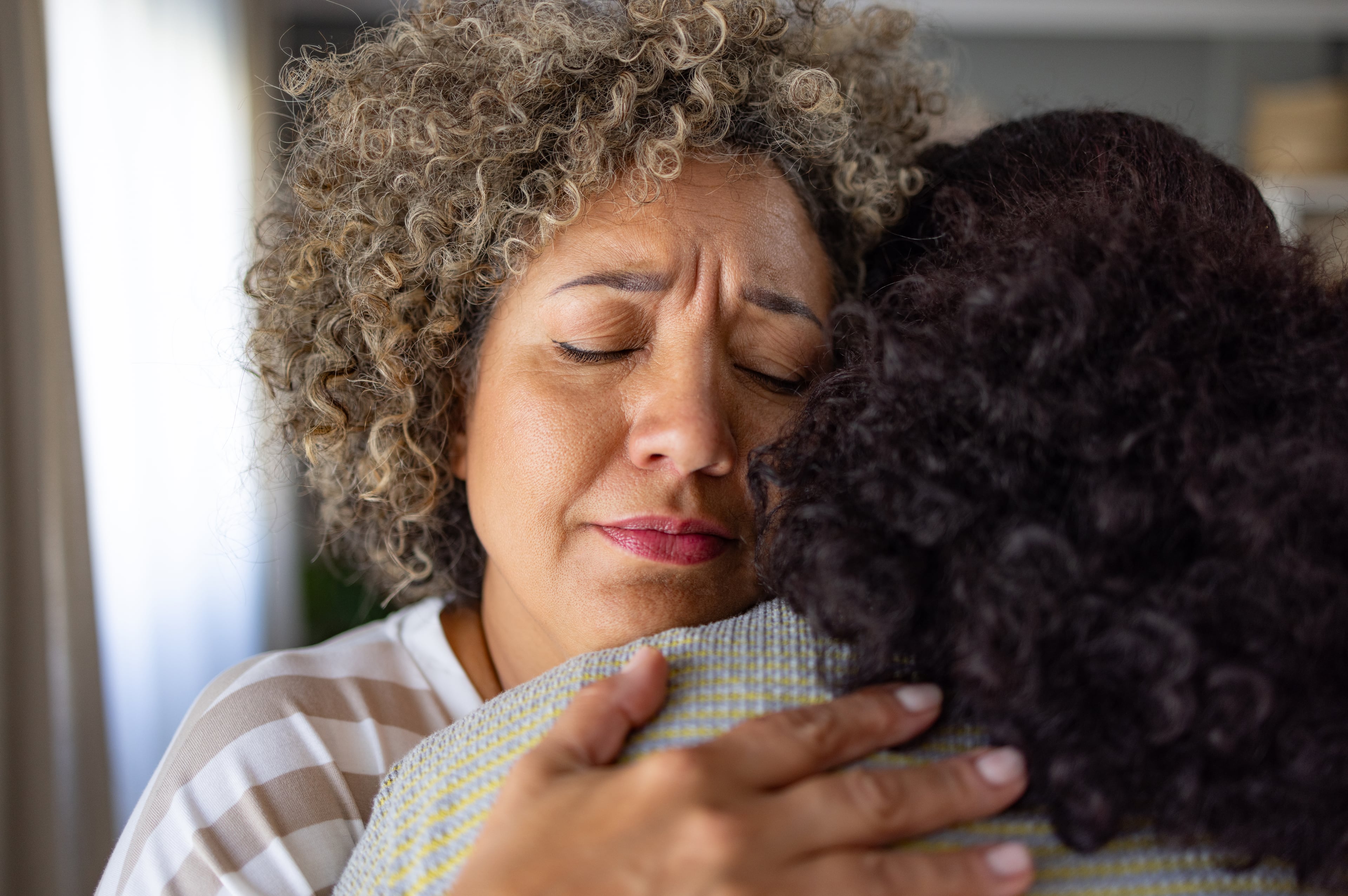 Worried mid adult woman embracing her friend at home.