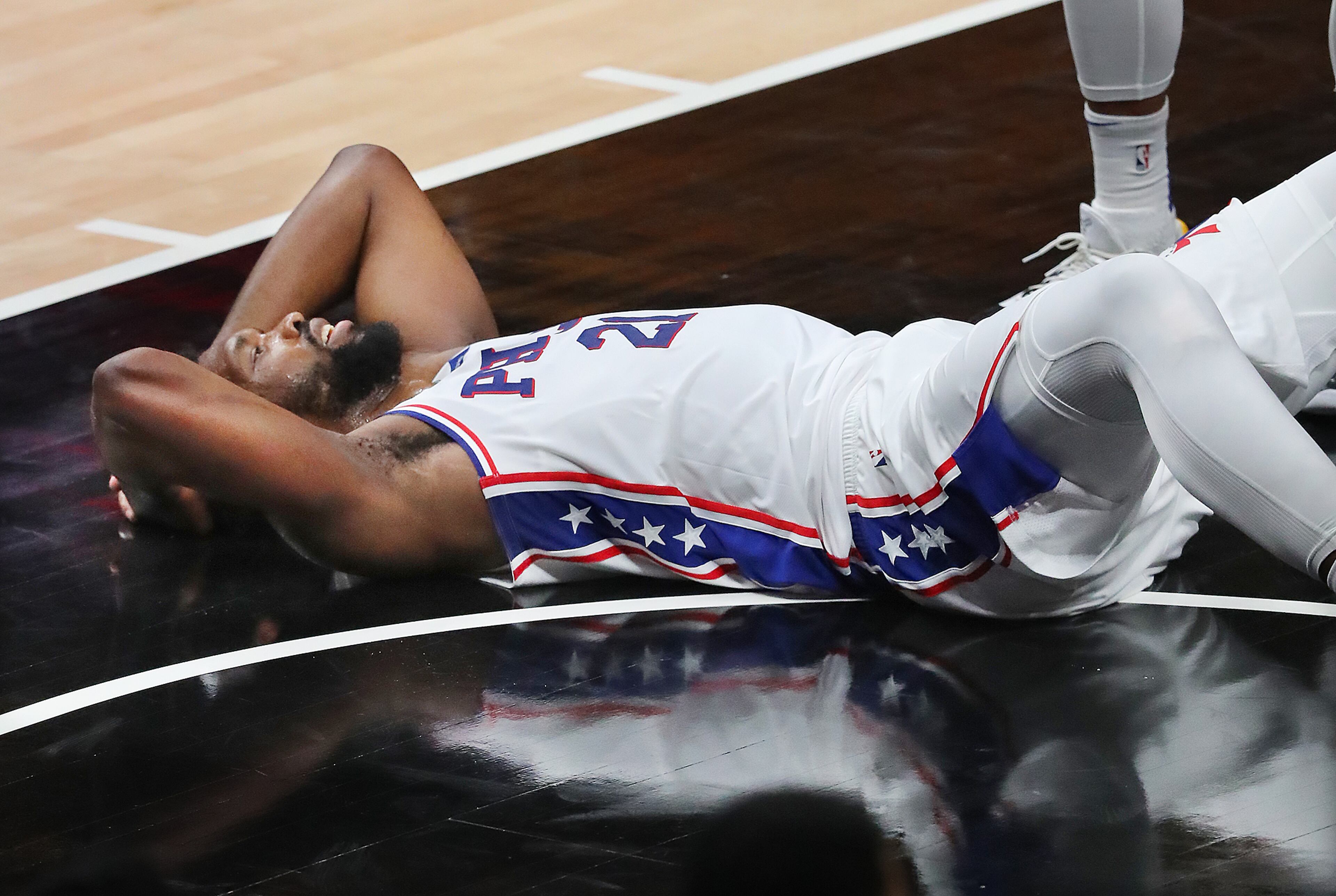 Philadelphia 76ers center Joel Embiid lays on the hardwood after a collision with Atlanta Hawks center Clint Capela. “Curtis Compton / Curtis.Compton@ajc.com”