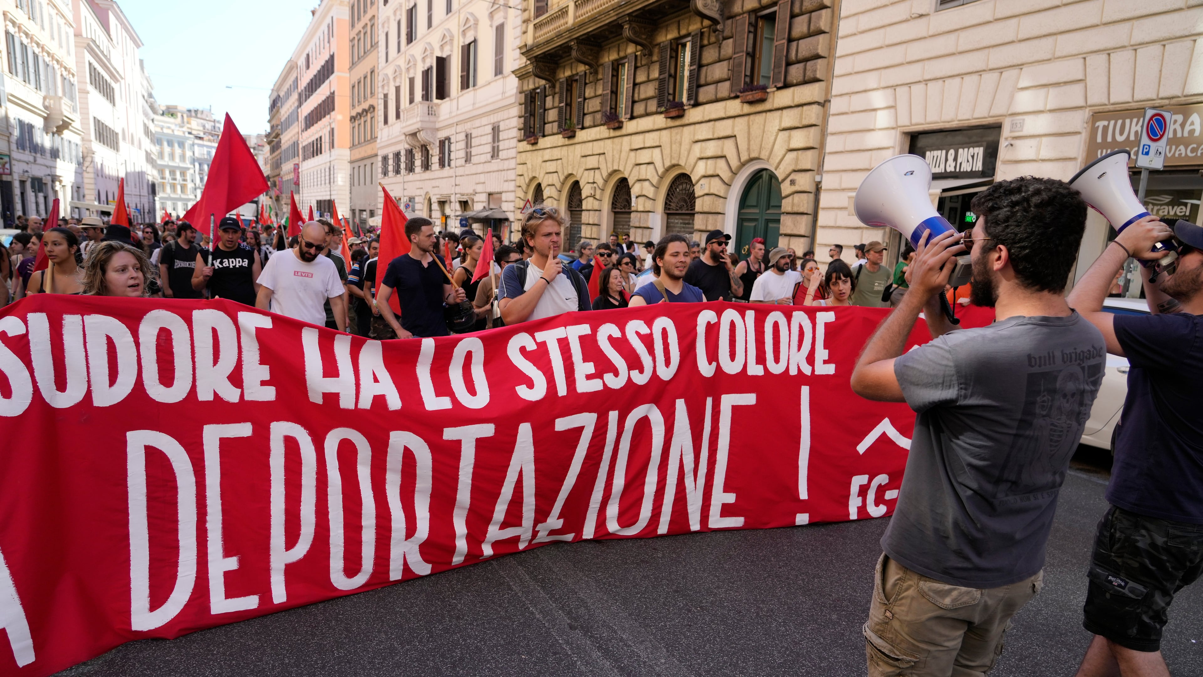 People hold a banner in Italian reading "Skin and sweat have the same color, no deportation' during a march in Rome, Saturday, June 13, 2026, to protest Italy's security and migration package, including a migrant "repatriation bonus" scheme criticized by opposition parties and legal groups as unconstitutional and ethically problematic. (AP Photo/Gregorio Borgia)