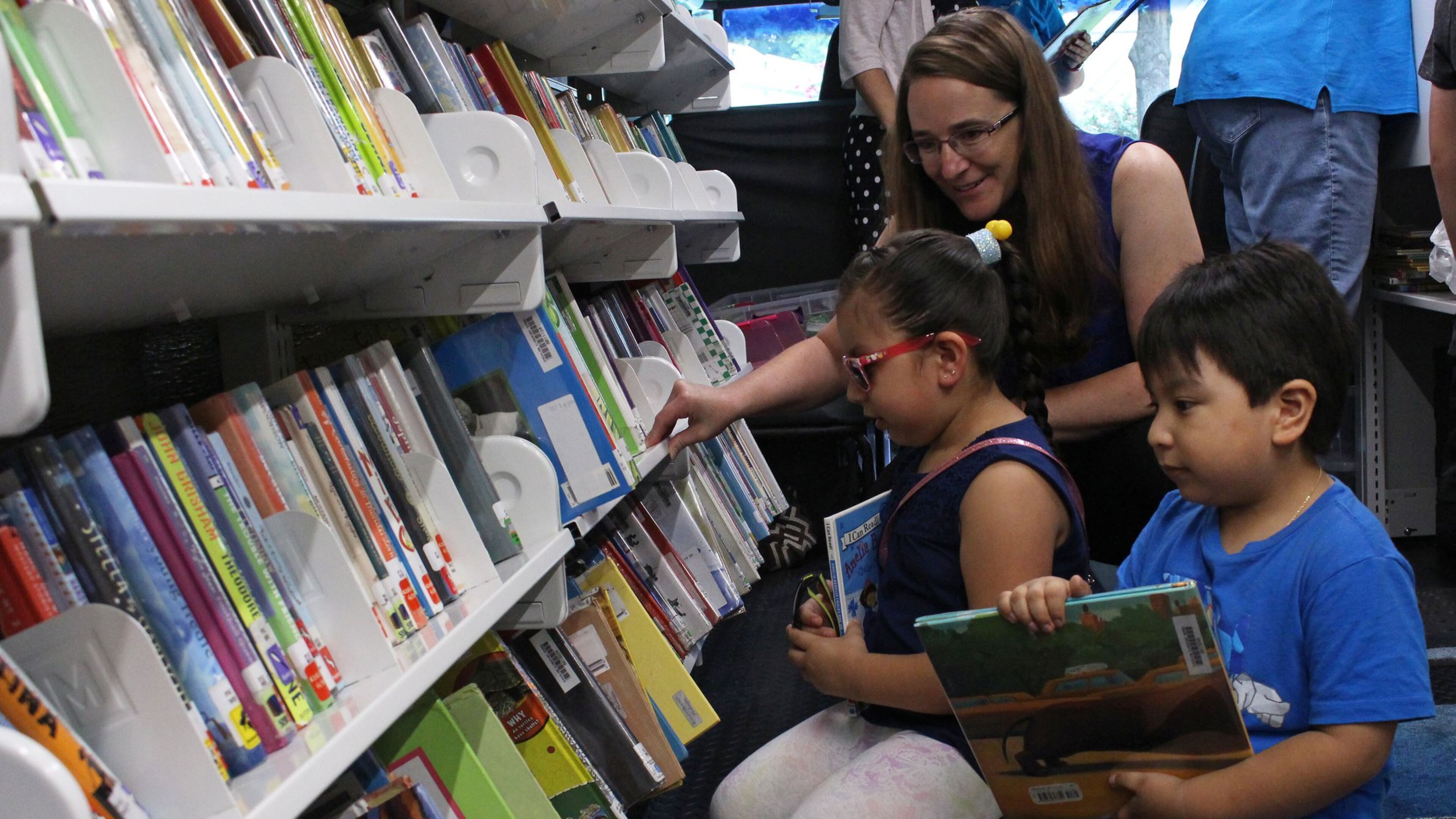 Claire Durbin, a special education kindergarten teacher, middle, helps Genesis Romero and Joushua Romero, left to right, find books on Gwinnett County Public Schools’ Book Mobile at the Centre at Peachtree Corners apartments on Friday, July 20. Gwinnett County Public Schools is holding its annual Child Find meeting Thursday for Gwinnett families whose children do not attend the public schools but might be eligible for special education services. Jenna Eason / Jenna.Eason@coxinc.com