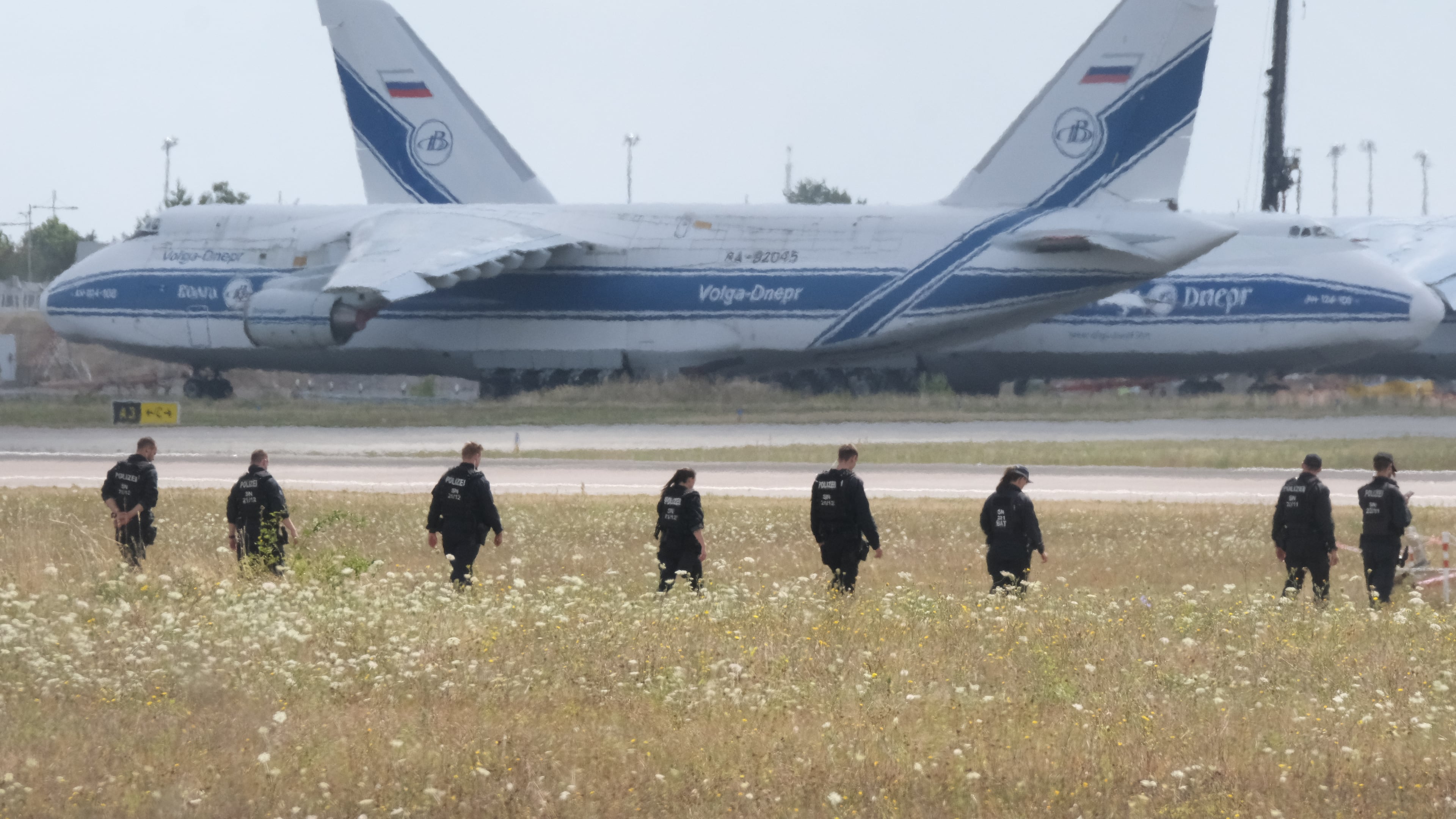 Police officers are walking across a field on the grounds of Leipzig Airport, in Schkeuditz, Germany, Friday, Aug. 7, 2026, searching for a drone that may be connected to a suspected attack. (Sebastian Willnow/dpa via AP)