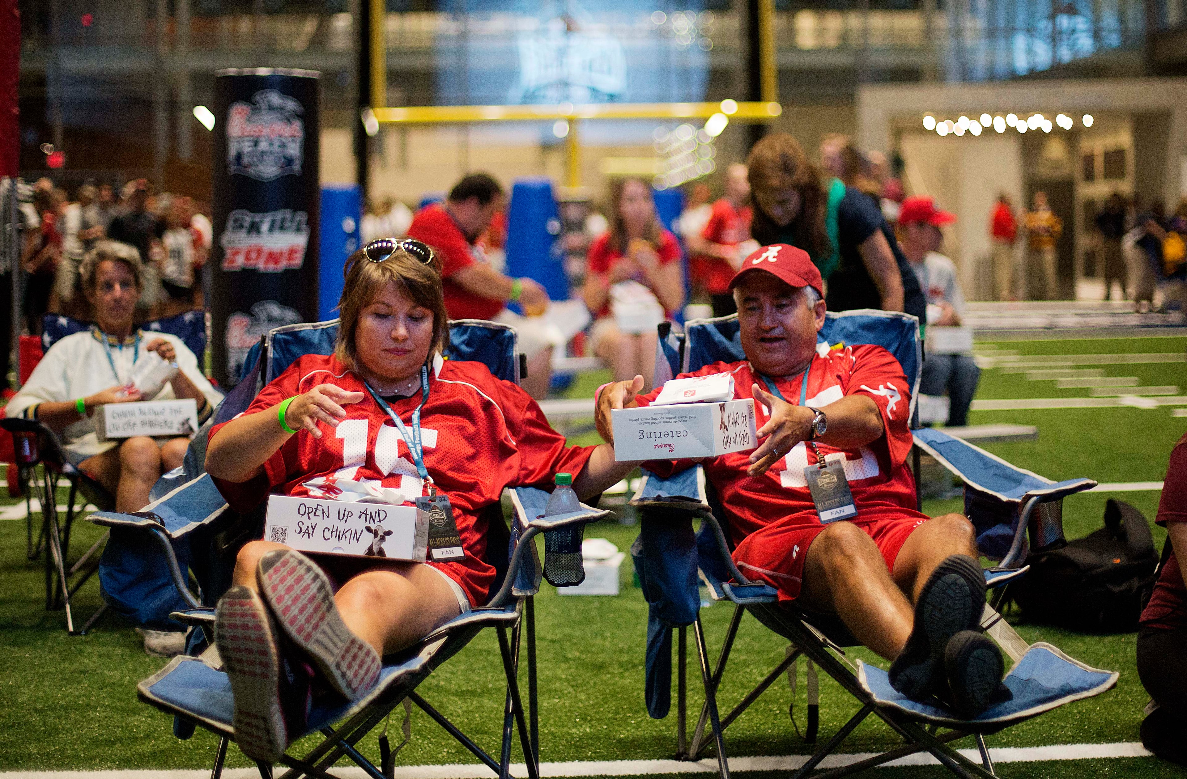 Amy, left, and Louis Valenzuela, of Marietta, Ga., sit down to eat dinner on the turf as part of a sleepover in the College Football Hall of Fame, Wednesday, Aug. 13, 2014, in Atlanta. "It's awesome," said Amy, an Alabama fan. "I think I already pulled my back but it's so much fun." (AP Photo/David Goldman)