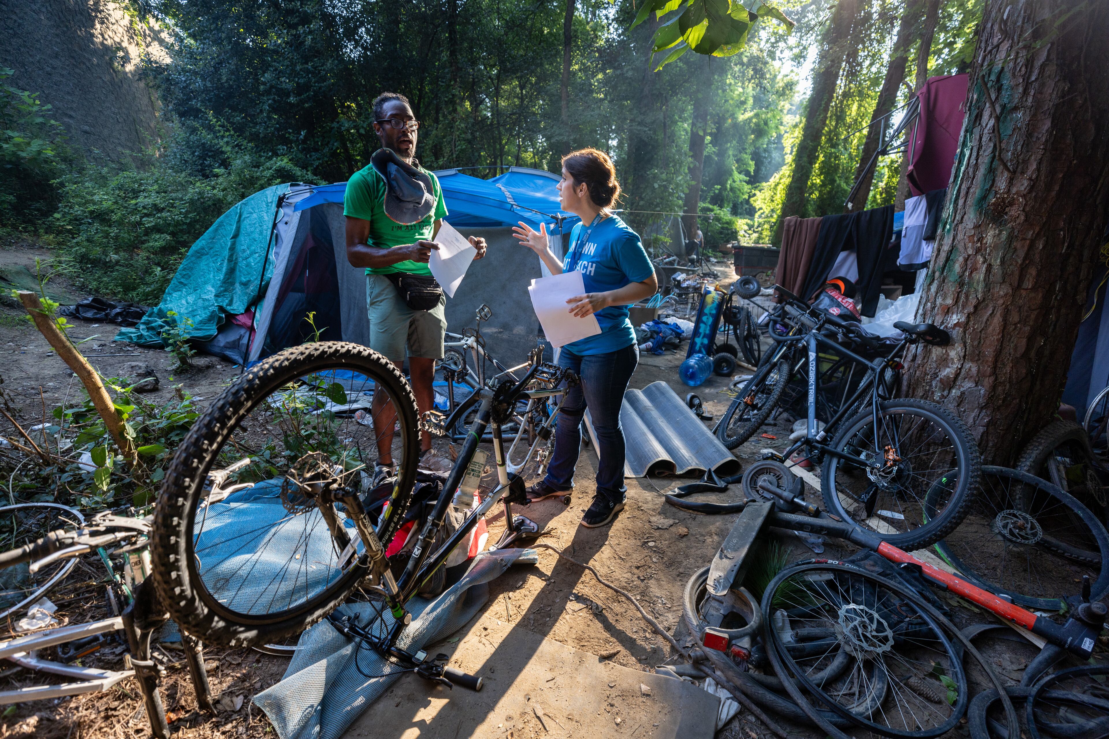 Intown Cares outreach representative Tracy Woodard talks with Ladell Hassell about an upcoming free medical care opportunity at a homeless encampment Along the banks of the North Fork of Peachtree Creek near Buford Highway, Tuesday, August 22, 2023. (Steve Schaefer/steve.schaefer@ajc.com)