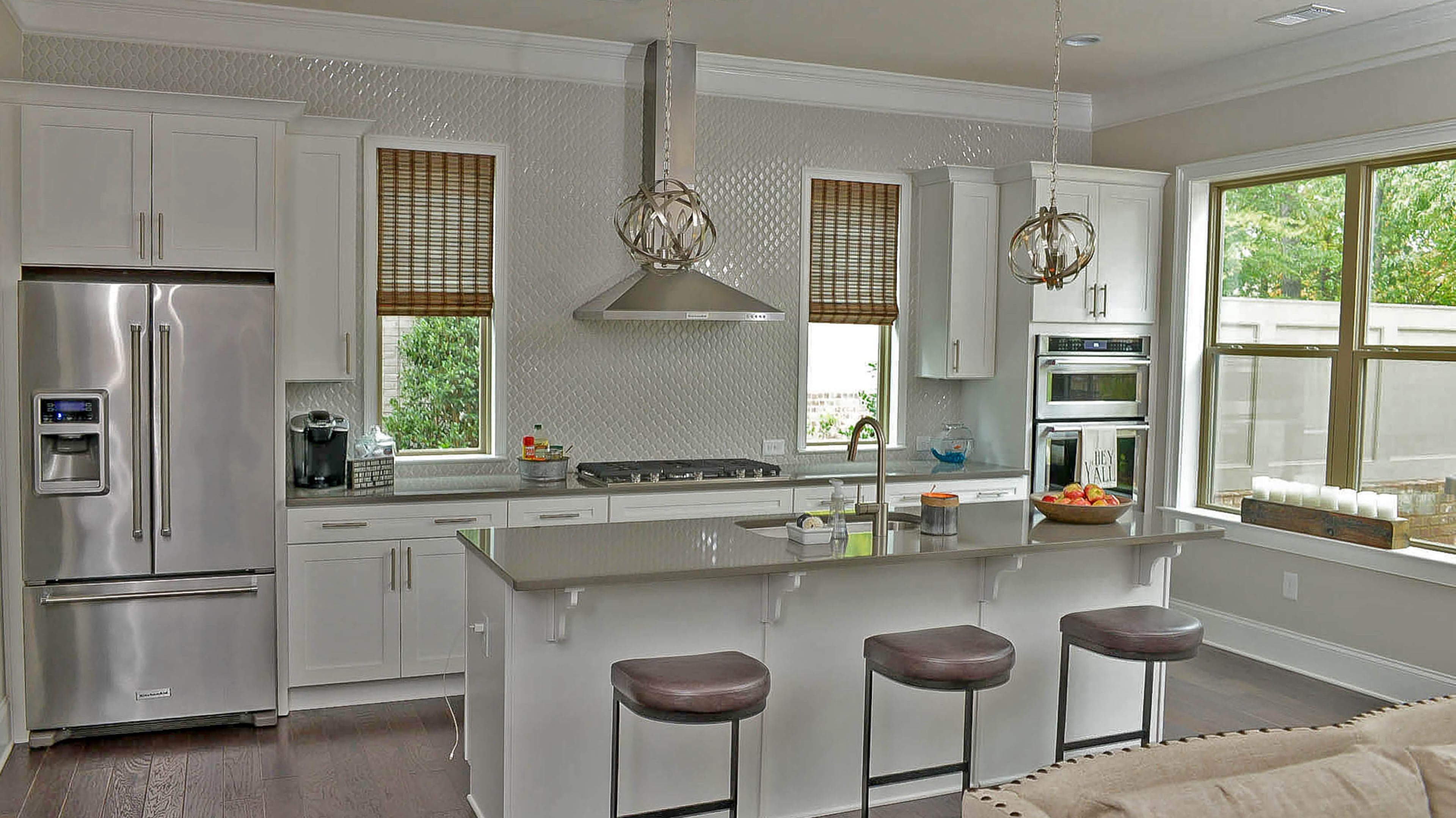 The glossy, white arabesque tile, a custom addition by Harvey, stands out against the stainless steel KitchenAid appliances and Capital Lighting spherical pendants. The hardwood floors are from Shaw.