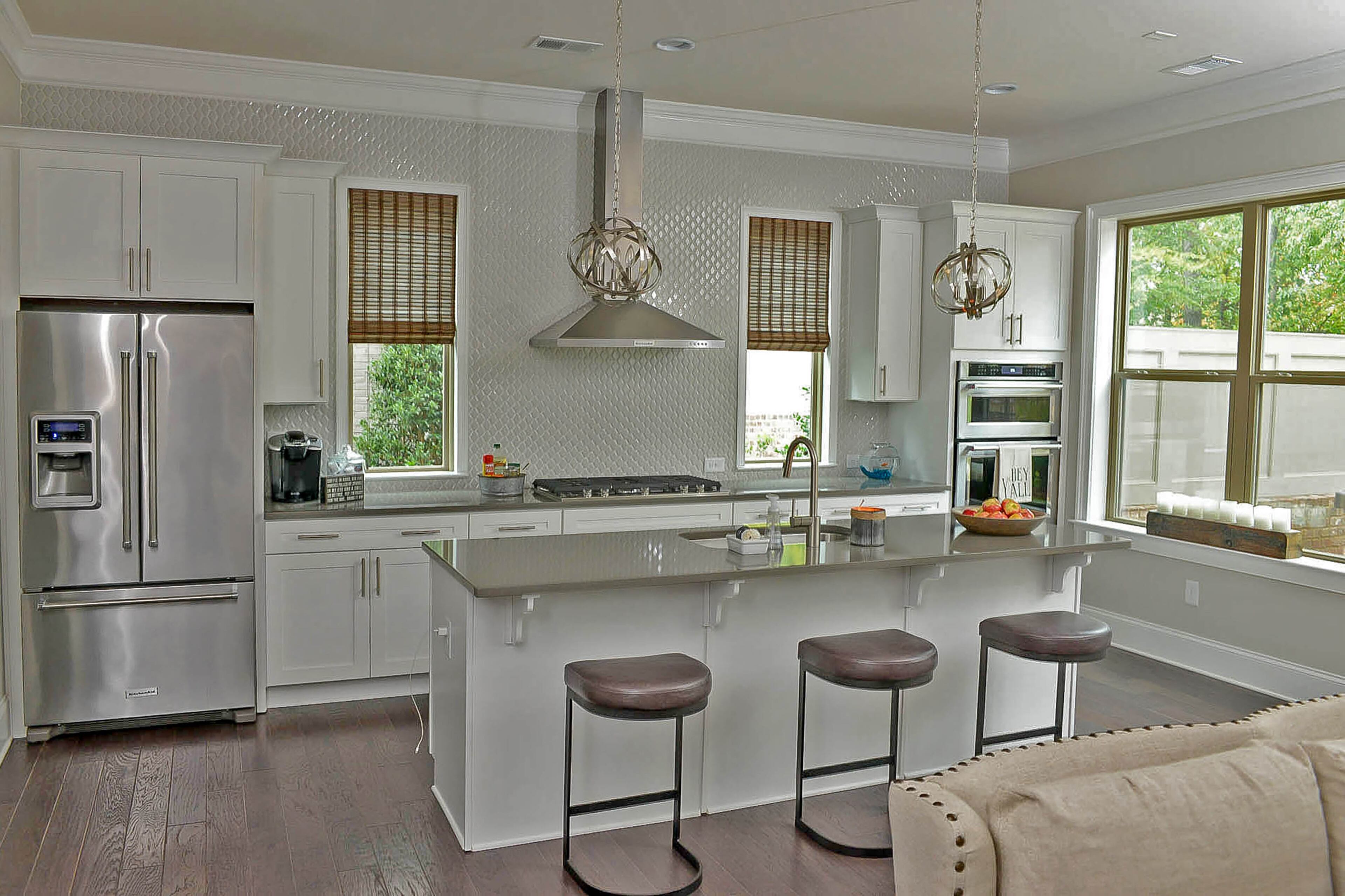 The glossy, white arabesque tile, a custom addition by Harvey, stands out against the stainless steel KitchenAid appliances and Capital Lighting spherical pendants. The hardwood floors are from Shaw.