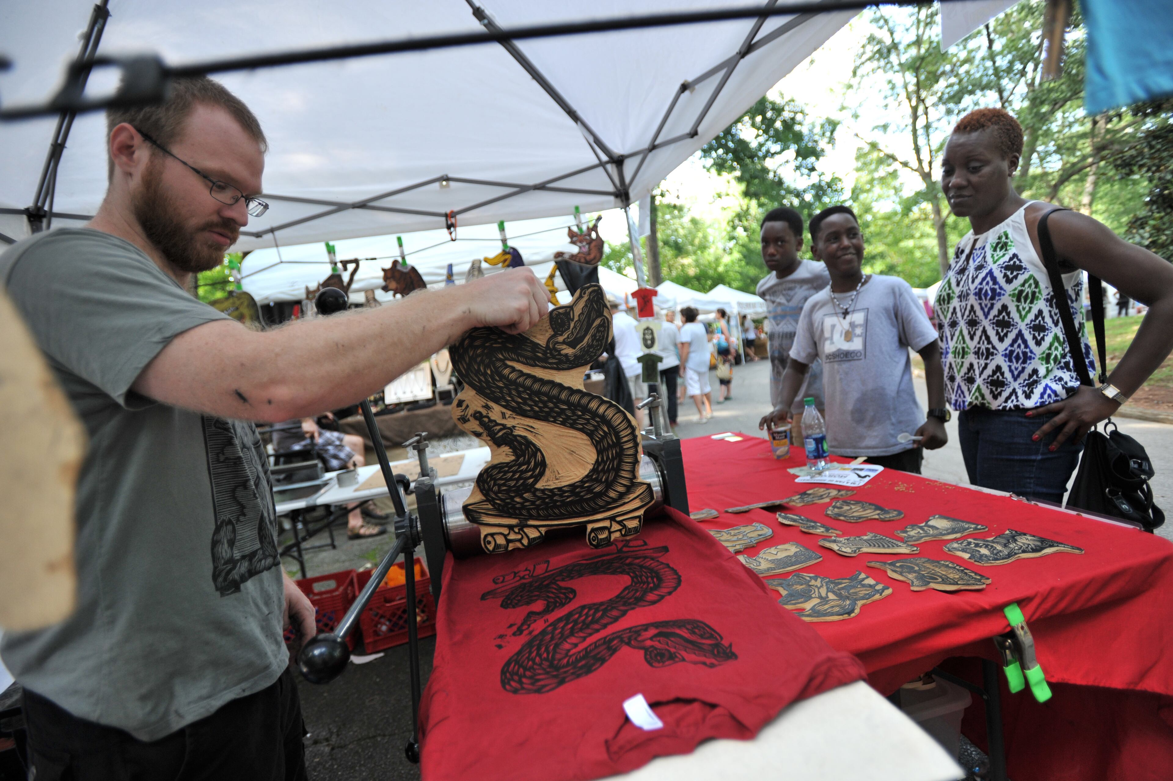 Artist Chris Neuenschwander (left) makes a hand printed t-shirt as Natasha Hyde (right), of Newnan, with her sons Samuel (second from right), 13, and Johari (third from right), 15, wait during Grant Park Summer Shade Festival on Saturday, August 24, 2013. The Grant Park Summer Shade Festival features an artist market, children's activities, great food, live music and the Adams Realtors 5K Run for the Park. The Children's Fun Center is a family favorite with storytellers, jugglers, sing-a-longs and kid-sized make-and-take projects. HYOSUB SHIN / HSHIN@AJC.COM