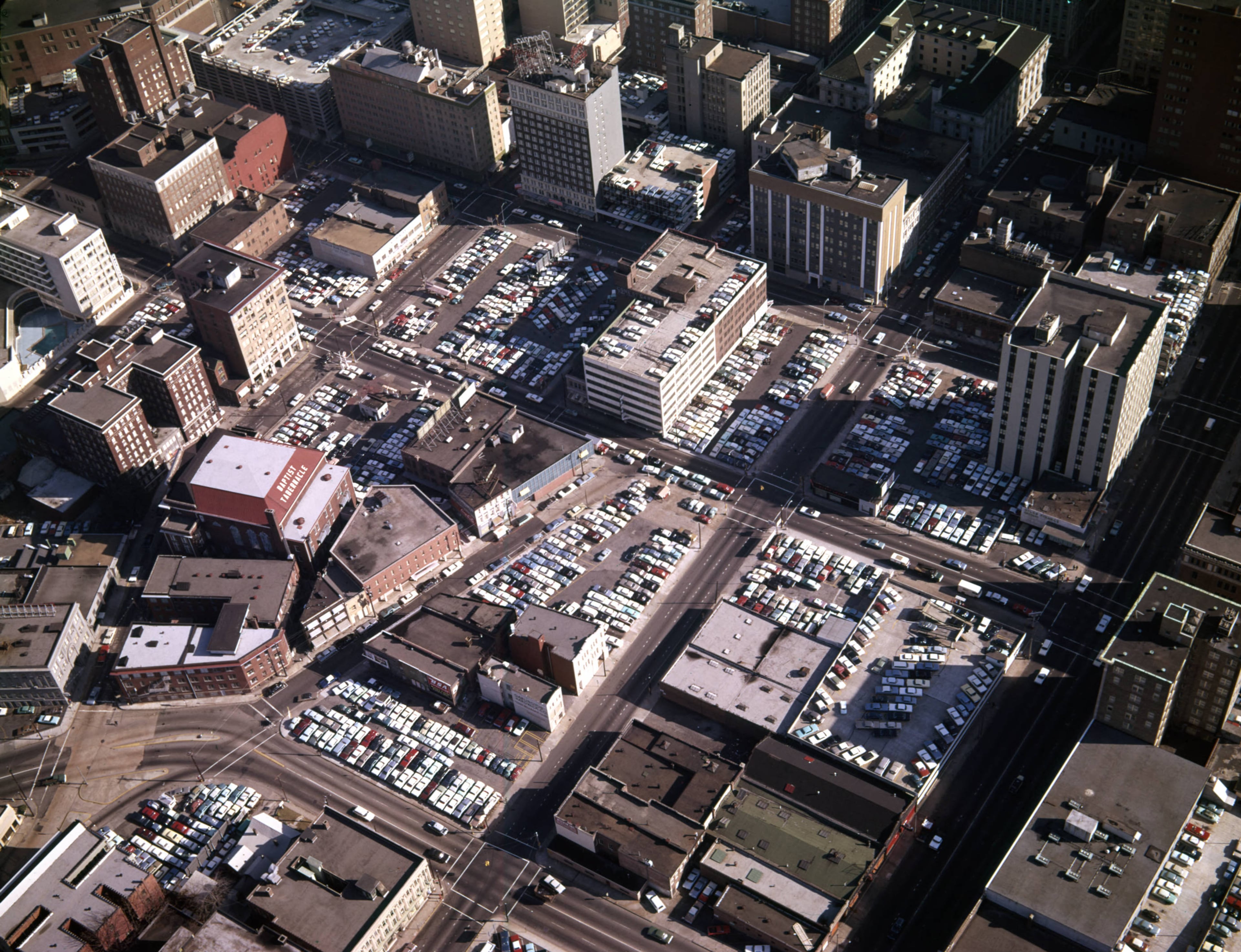 Aerial view of downtown, looking northeast, showing large areas covered in parking lots, Atlanta, Georgia, December 21, 1965. "Atlanta Parking Lots and Shopping Centers. 12-21-65. F. Jillson. From the negative envelope: " Marietta Street is the large street running diagonally from the bottom right corner. The first intersection we see is at Spring Street. Note the Baptist Tabernacle, today known as The Tabernacle, a music venue. The future site of Centennial Towner is in the top right corner. Floyd Jillson/AJC