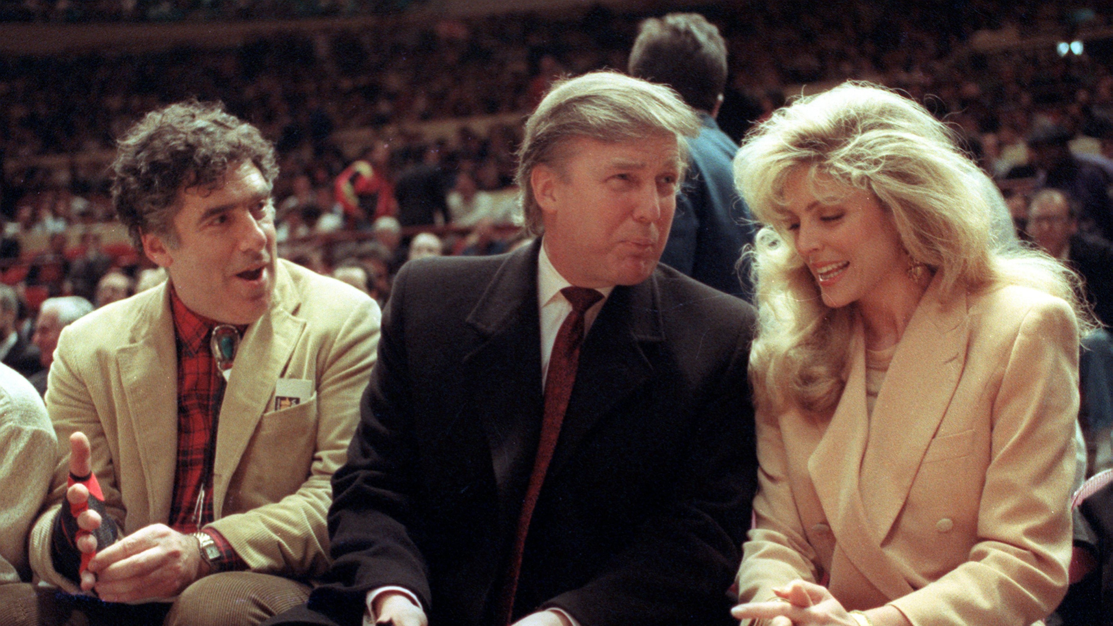 FILE - Actor Elliott Gould, left, joins Donald Trump, center, and Marla Maples at courtside during an NBA basketball game between the Phoenix Suns and the New York Knicks at Madison Square Garden, in New York, March 6, 1991. (AP Photo/Steve Freeman, File)