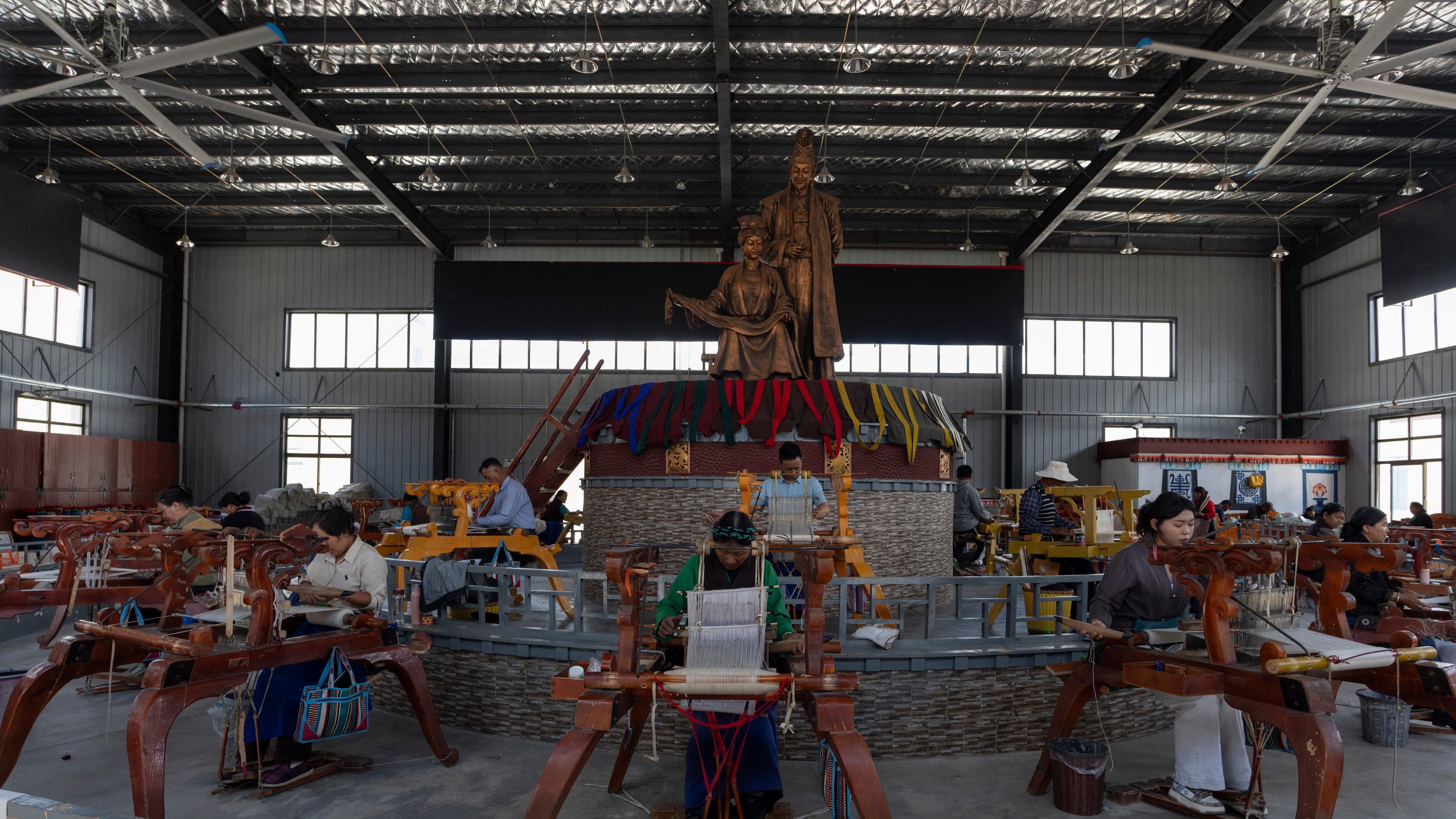 Workers weave Pulu, a traditional wooden fabric into clothing, at wooden looms near statues of Princess Wencheng and Tibetan King Songtsen Gampo at the Ethnic Huaji Handwoven Cooperative in Shannan in western China's Tibet Autonomous Region on July 23, 2026, as seen during a government organized visit for foreign journalists. (AP Photo/Ng Han Guan)