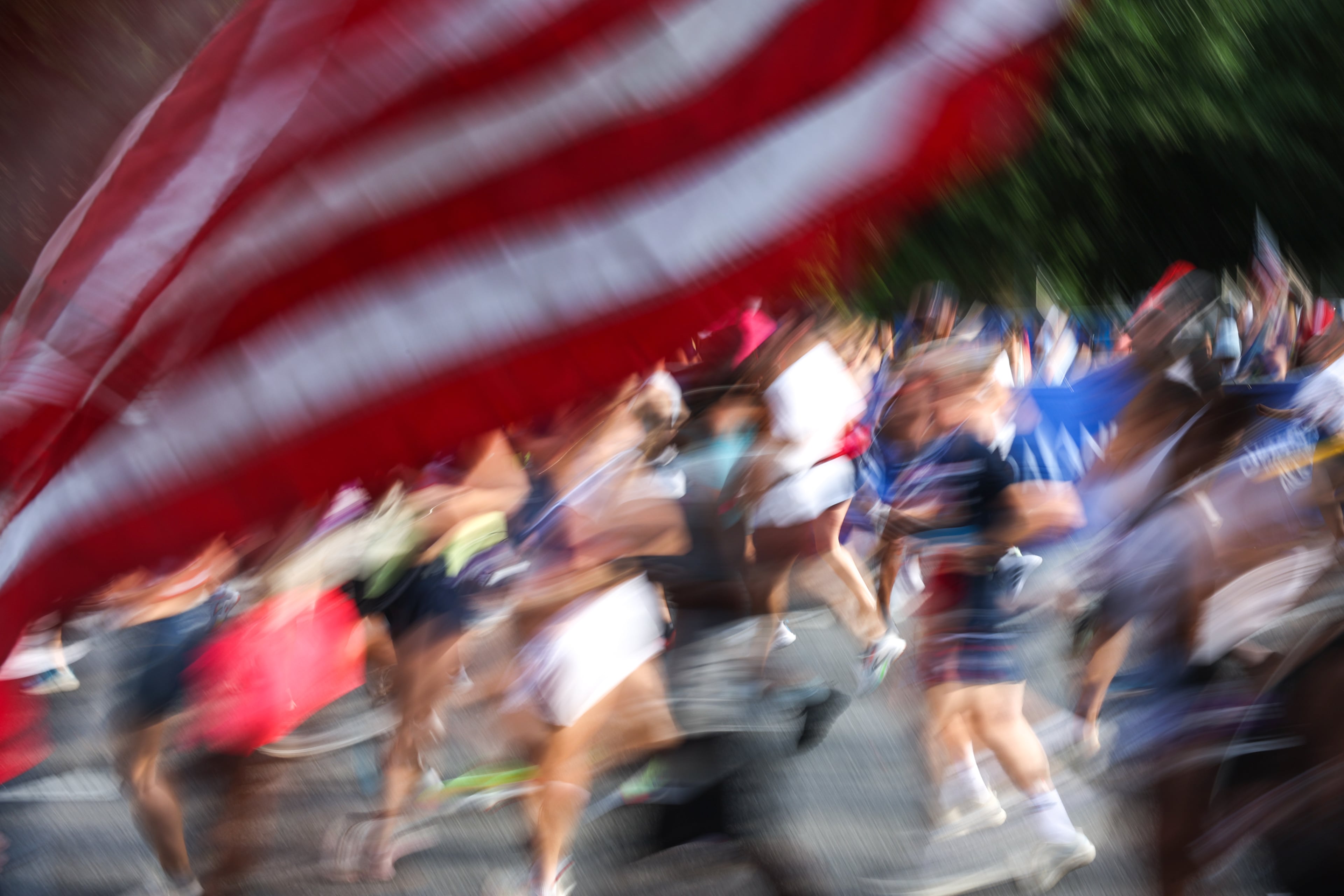 Participants run past a flag during the 57th running of the Peachtree Road Race on Saturday, July 4, 2026, in Atlanta. (Arvin Temkar/AJC)