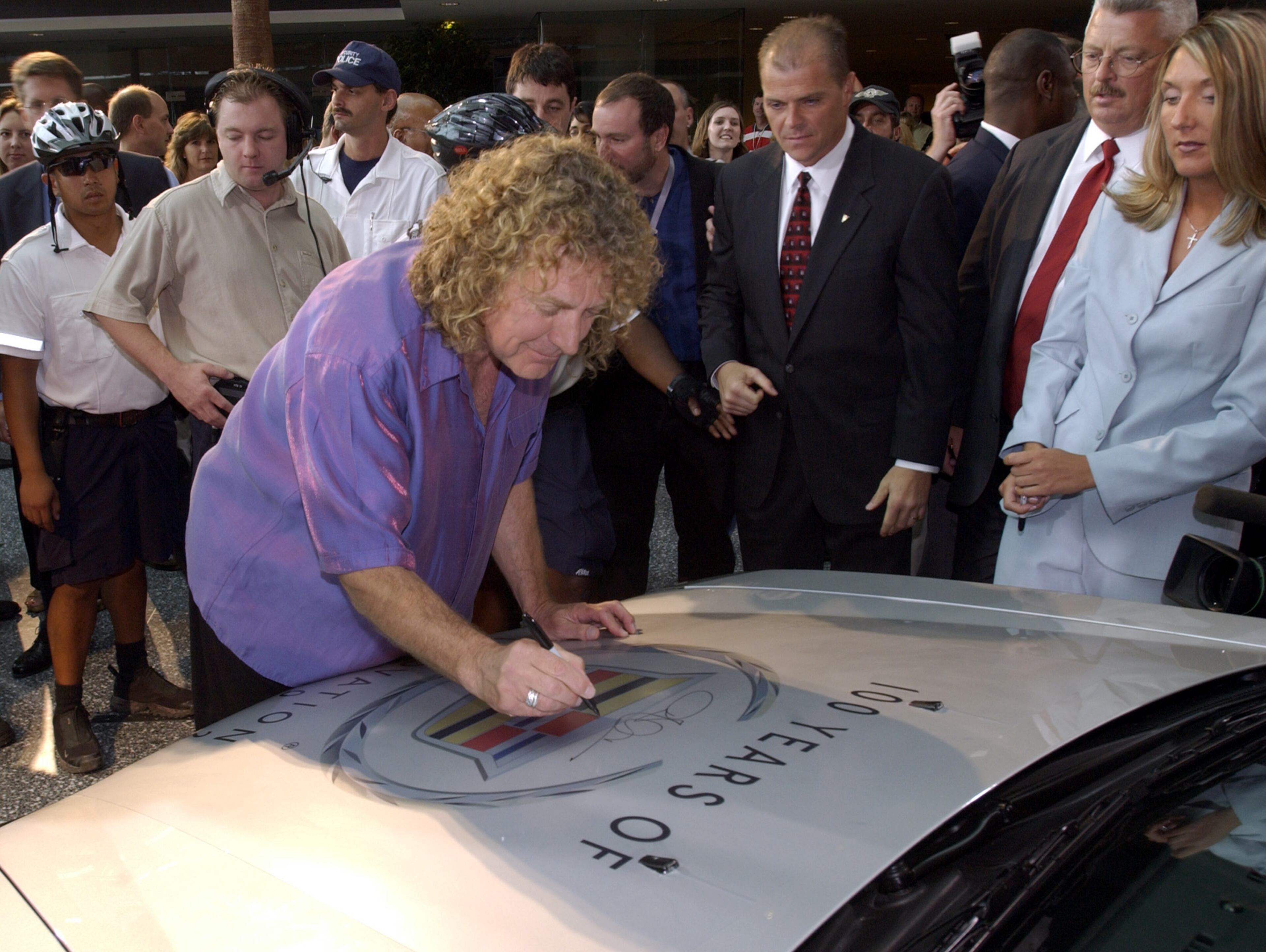 Robert Plant, of the rock band Led Zeppelin autographs the hood of a Cadillac CTS at General Motors' headquarters in Detroit, Mich., to help celebrate Cadillac's 100th birthday, Thursday, Aug. 22, 2002. The band's song 'Rock and Roll' was featured in Cadillac television advertising. At center right watching is Cadillac General manager Mark LaNeve. (AP Photo/General Motors, Blake J. Discher)