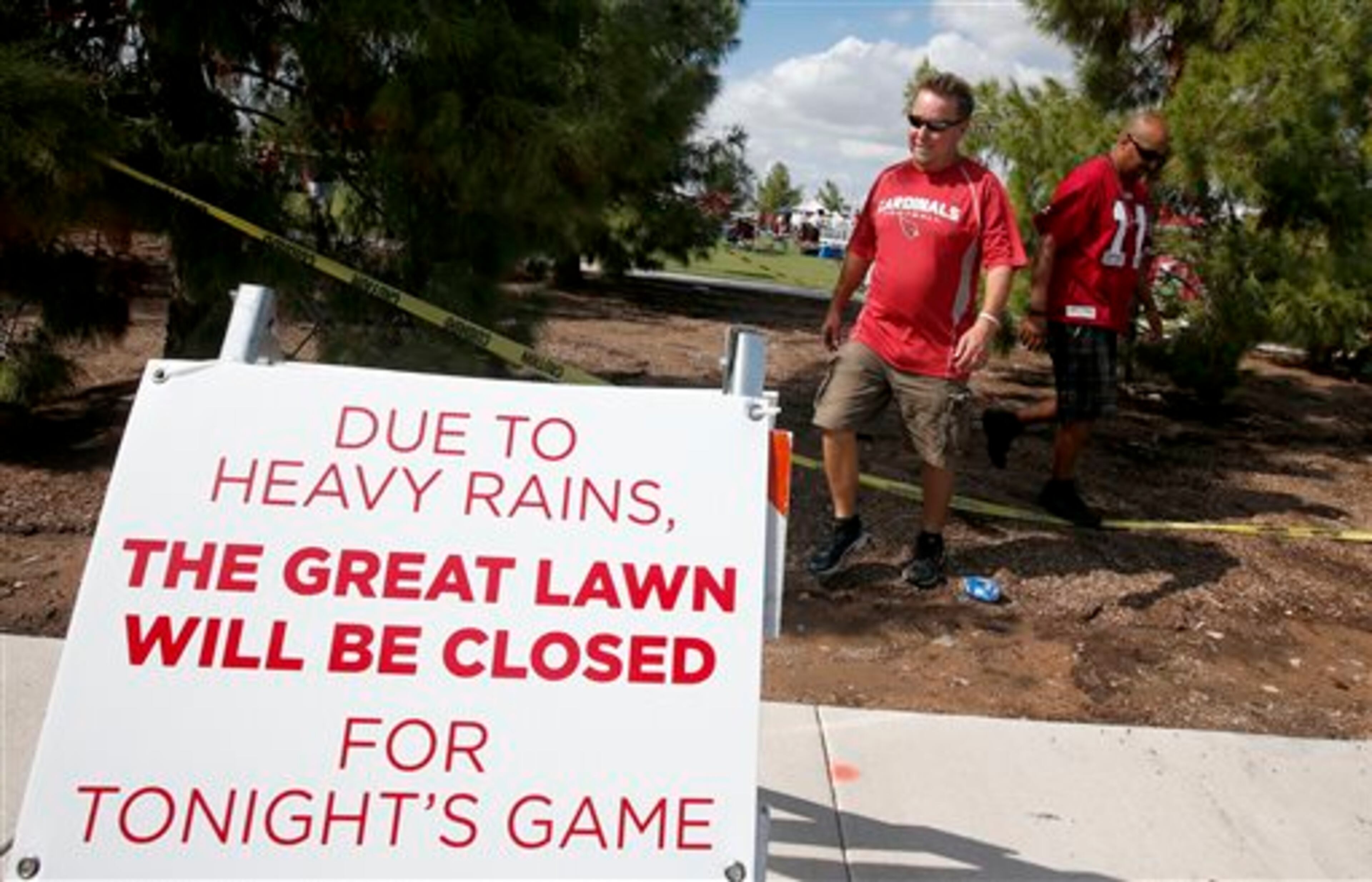 Arizona Cardinals fans walk past a sign and tape blocking off the official tailgating area as fans set up in the closed area anyway prior to an NFL football game San Diego Chargers Monday, Sept. 8, 2014, in Glendale, Ariz. Record breaking rains caused major flooding, closing roads and schools in the metro area. (AP Photo/Ross D. Franklin)