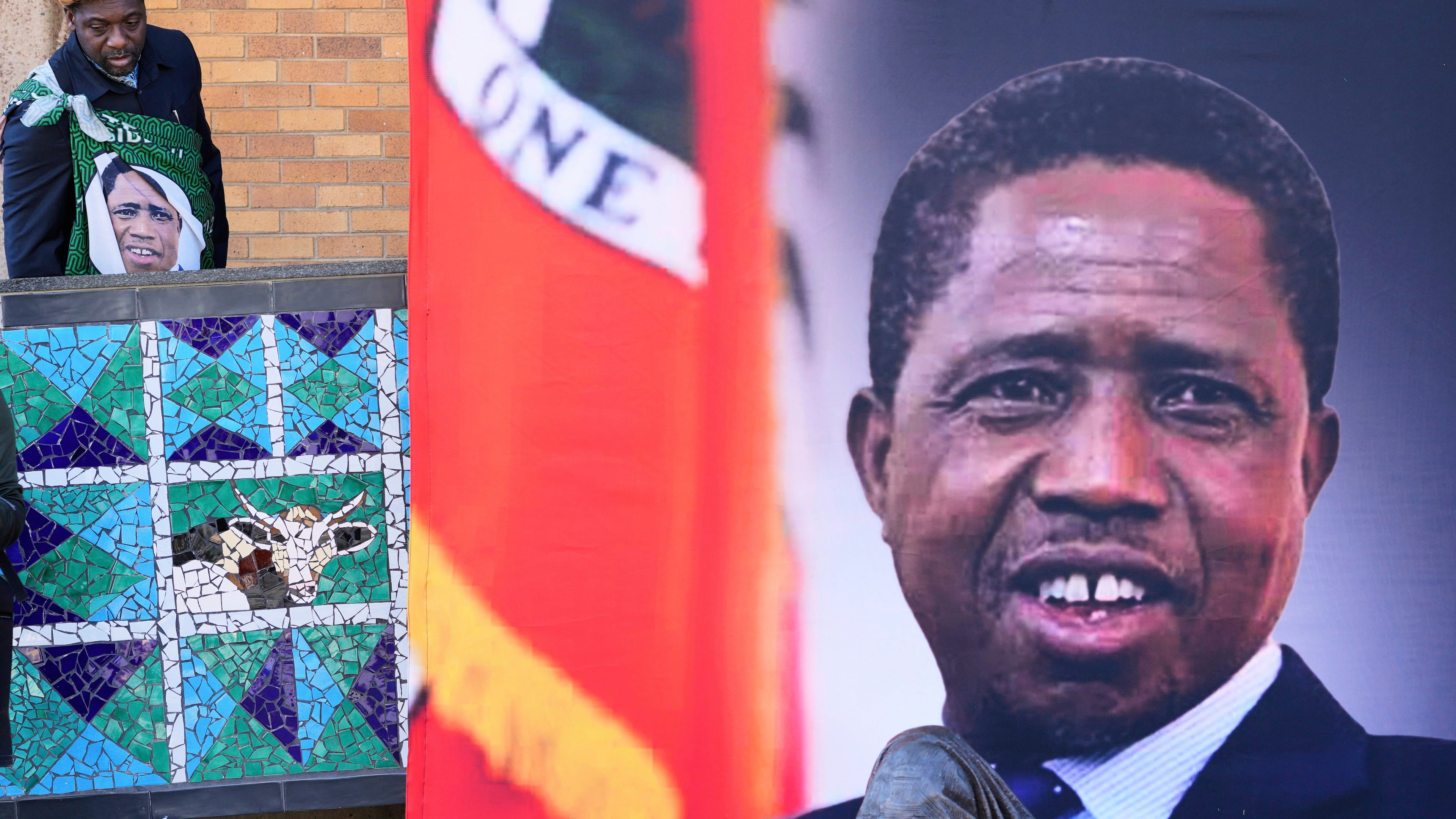FILE -A supporter arrives for a Mass for former Zambian President Edgar Lungu, shown in a banner at right, at the Cathedral of Christ the King in Johannesburg, South Africa, June 25, 2025. (AP Photo/Themba Hadebe, File)