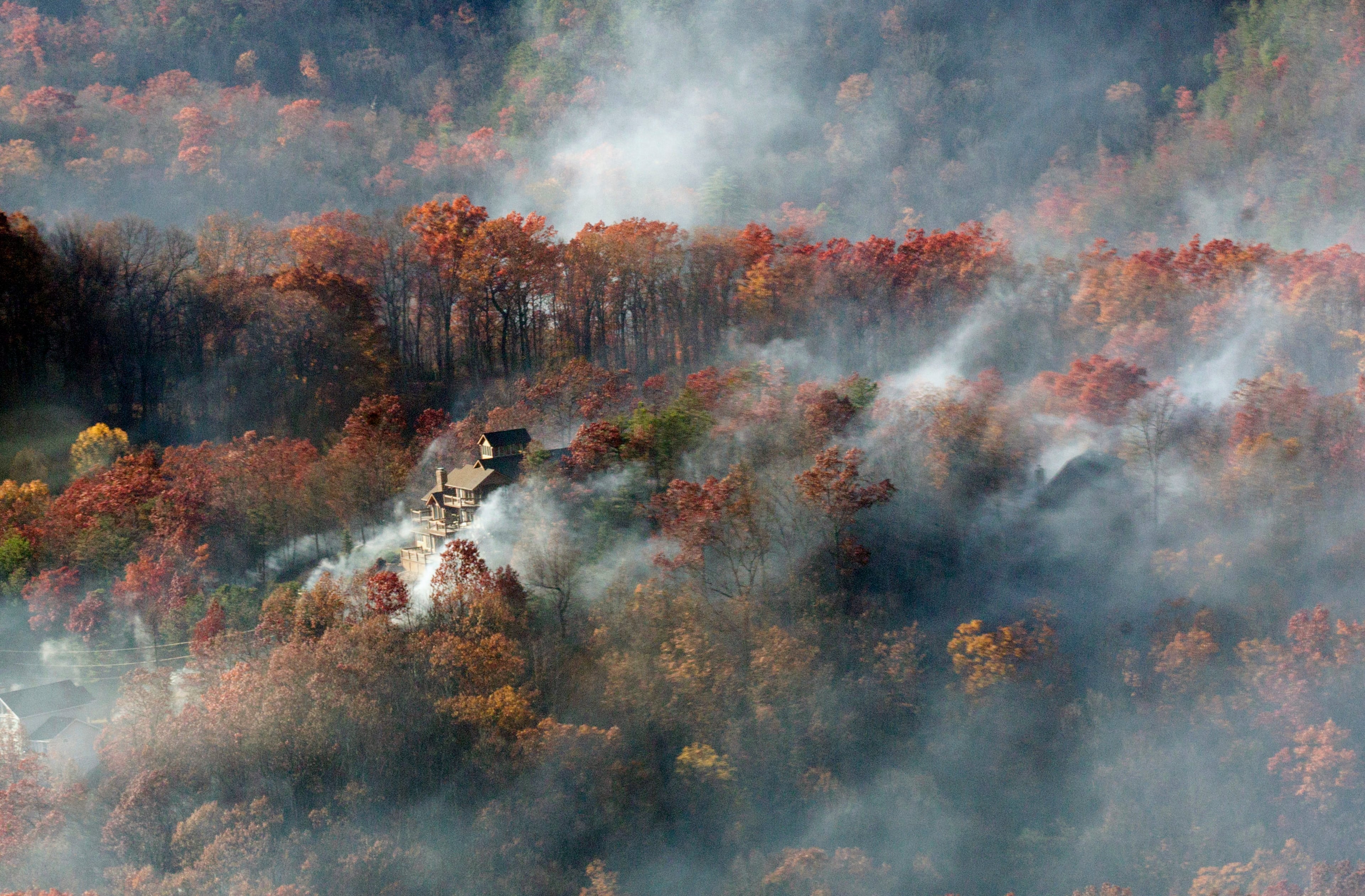 Smoke surrounds a home as seen from aboard a National Guard helicopter near Gatlinburg, Tenn., Tuesday, Nov. 29, 2016. Thousands of people have fled deadly wildfires that have destroyed hundreds of homes and a resort in the Great Smoky Mountains. (AP Photo/Erik Schelzig)