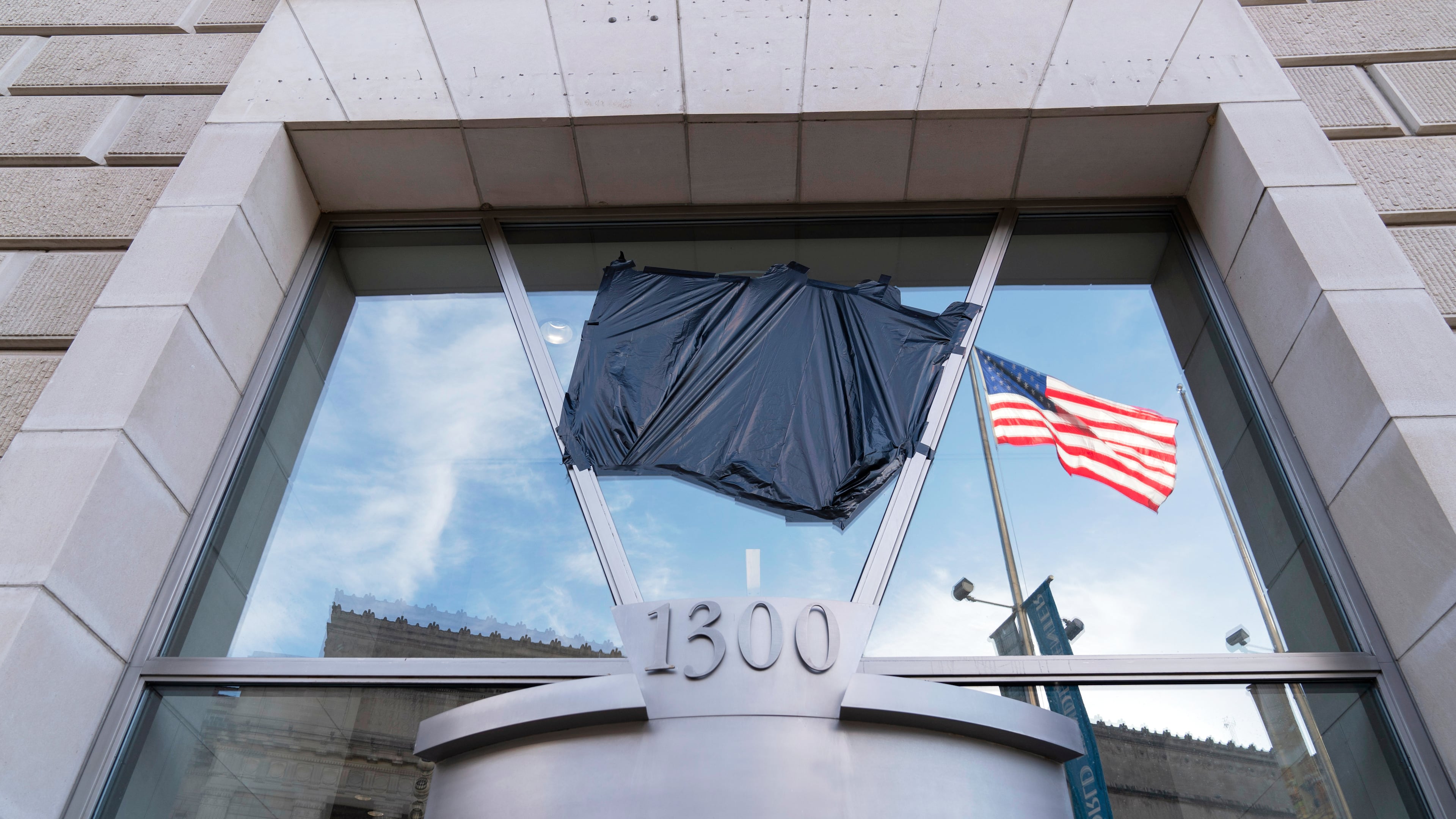FILE - The American flag flying alone beside an empty flagpole that previously had the flag of the U.S. Agency for International Development, or USAID, are pictured in the reflection of a window that previously had the sign and the seal of USAID, outside the agency's headquarters in Washington, Feb. 7, 2025. (AP Photo/Jose Luis Magana, File)