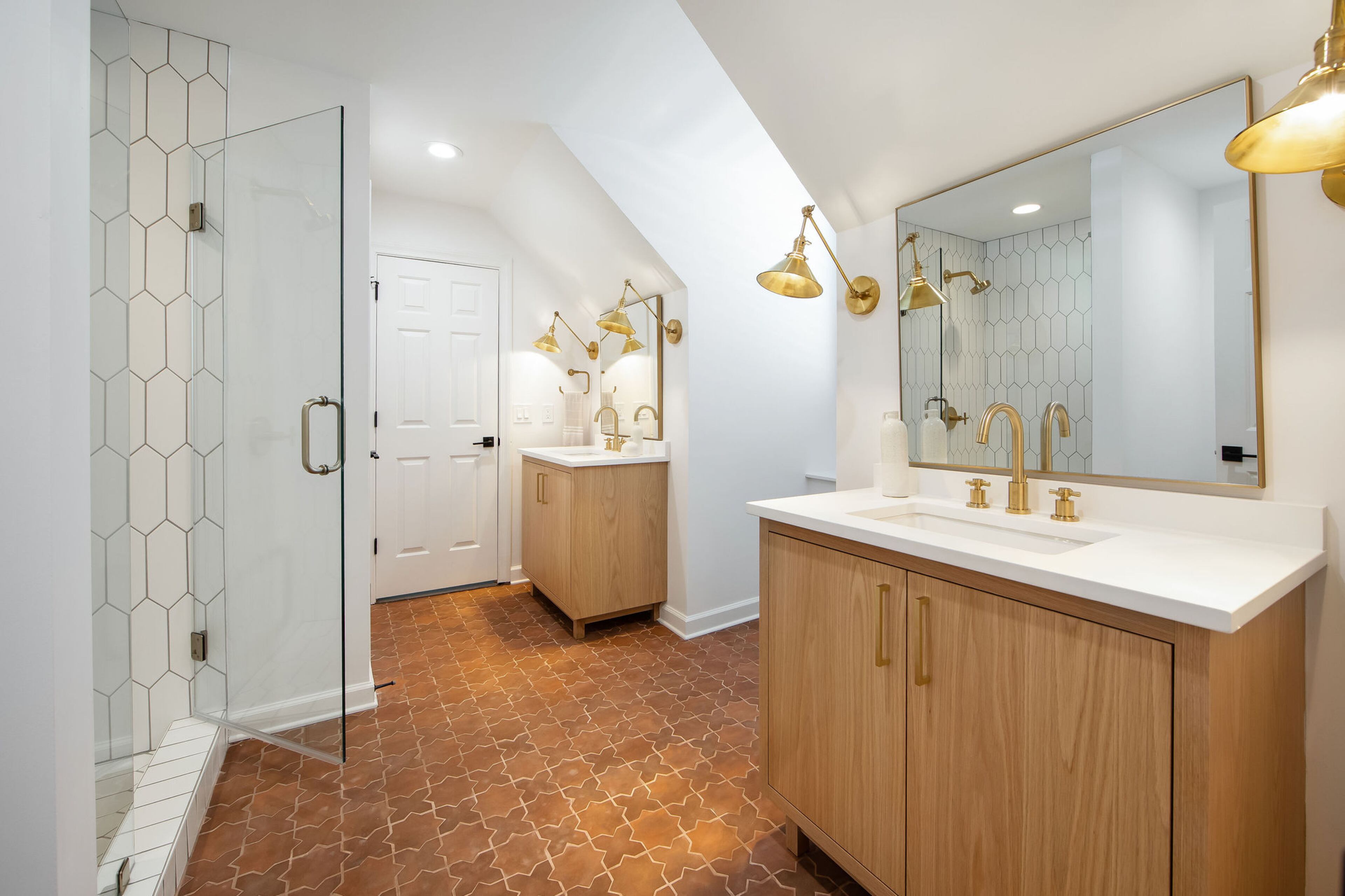 This jack-and-jill bathroom connects two guest rooms on the top floor. Terracotta clay tiles from Tierra y Fuego form a motif on the floors, contrasted with white Floor and Decor tiles in the shower. Golden fixtures — like the CB2 mirrors, Kohler plumbing, and custom sconces — polish off the space. Text by Lori Keong/Photo by Amanda Winchester