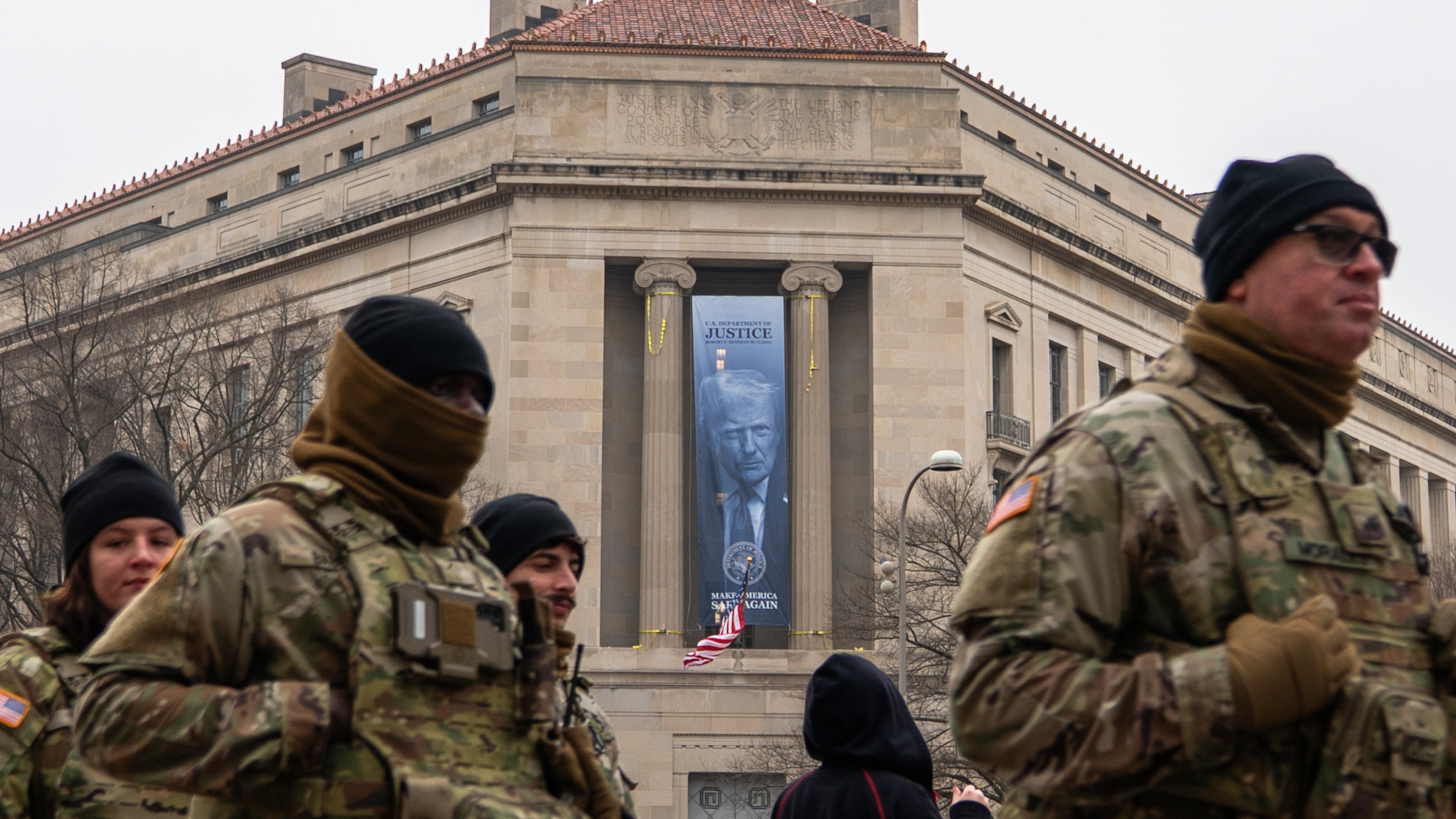 Members of the National Guard walk past a banner with President Donald Trump hanging on the Department of Justice, Thursday, Feb. 19, 2026, in Washington. (AP Photo/Allison Robbert)