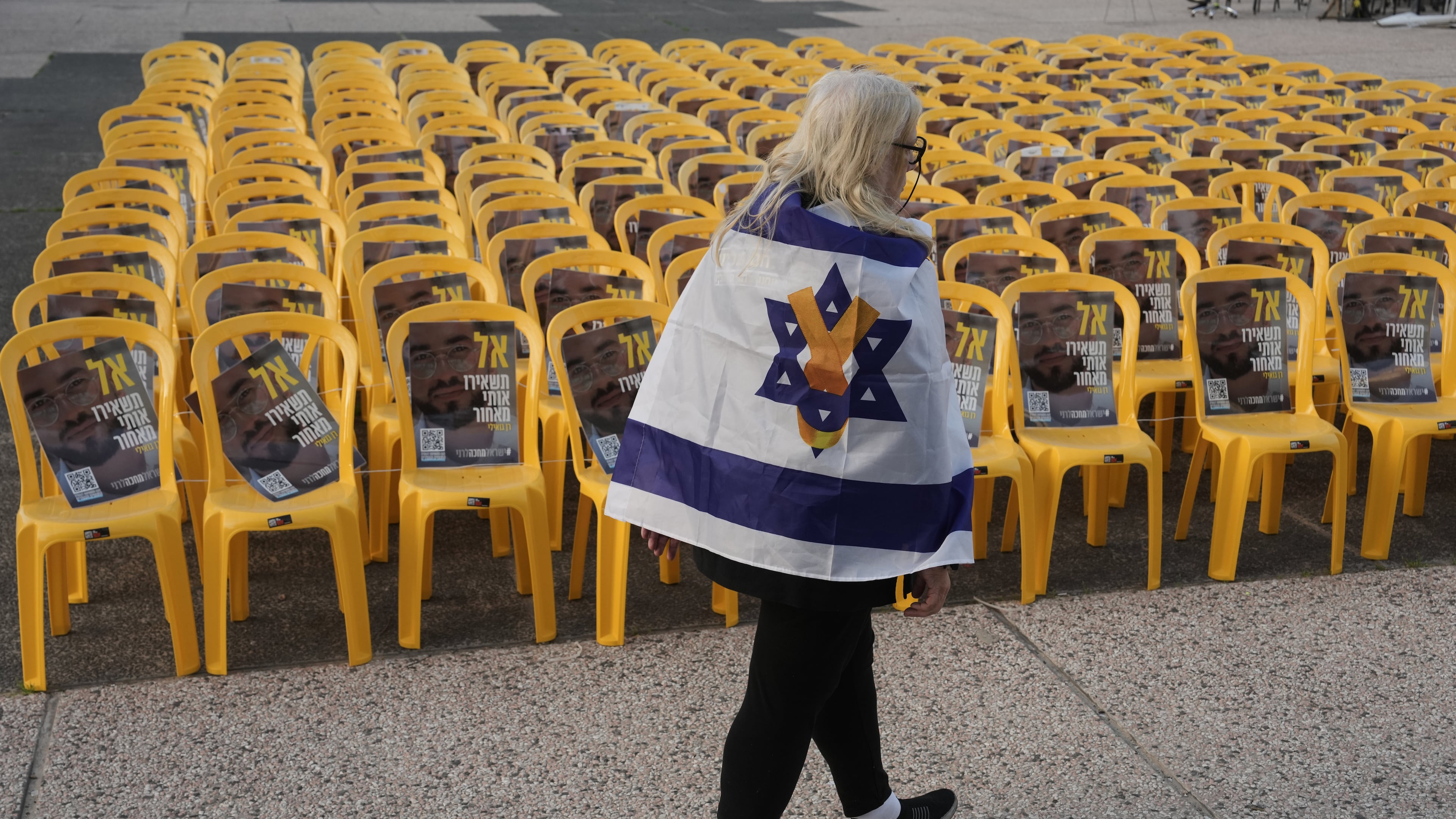 A woman walks by chairs with photos of Ran Gvili, the final hostage in Gaza who was killed while fighting Hamas militants during the Oct. 7, 2023 attack and whose remains have been recovered Monday, clearing the way for the next phase of the ceasefire that paused the Israel-Hamas war, in a plaza known as Hostages Square in Tel Aviv, Israel, Monday, Jan. 26, 2026. (AP Photo/Oded Balilty)