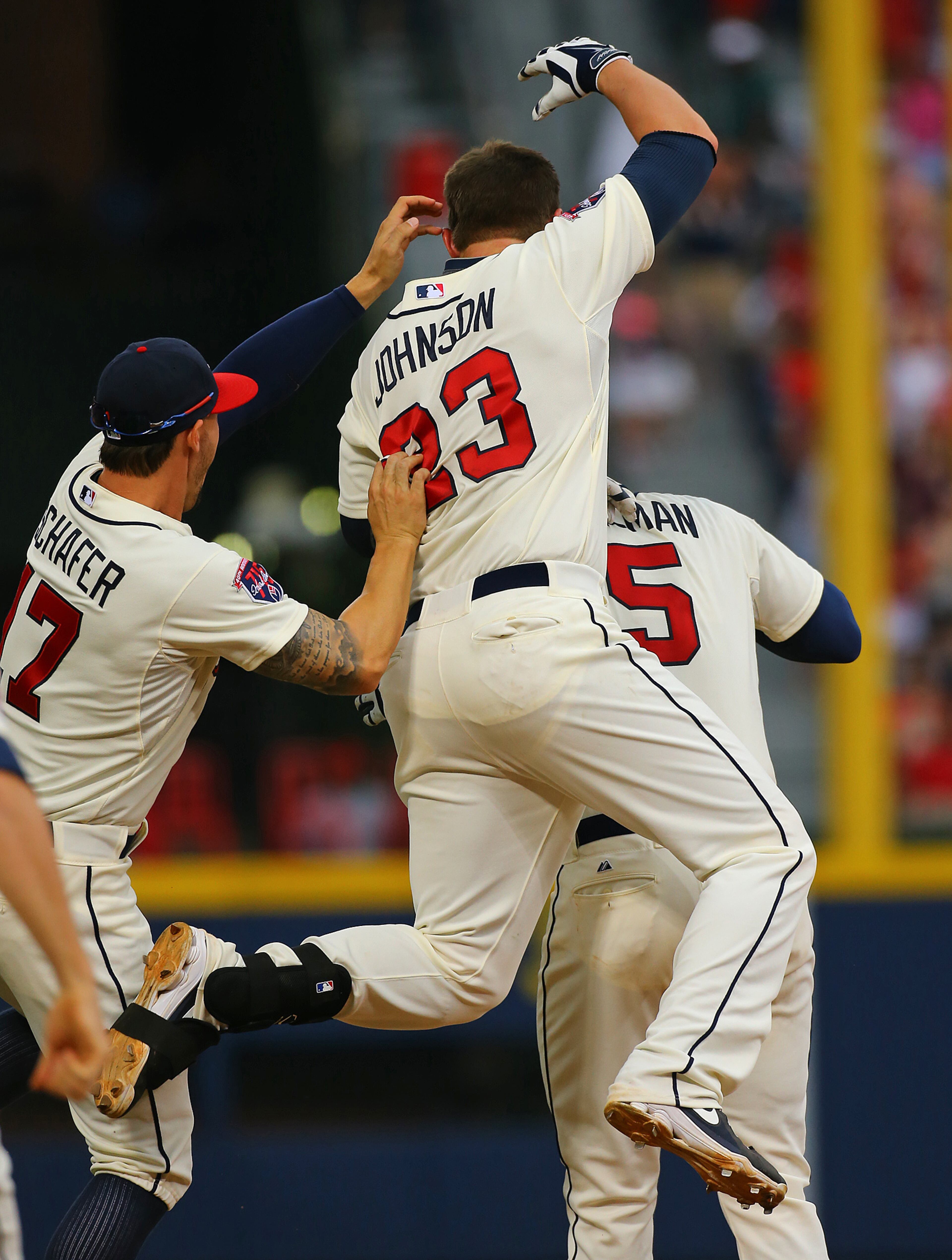 Jordan Schafer (left) and Chris Johnson jump on Freddie Freeman (right) after Freeman hit a game-winning RBI single to beat the Reds 1-0 in the 10th inning of their MLB baseball game in Atlanta. CURTIS COMPTON / CCOMPTON@AJC.COM