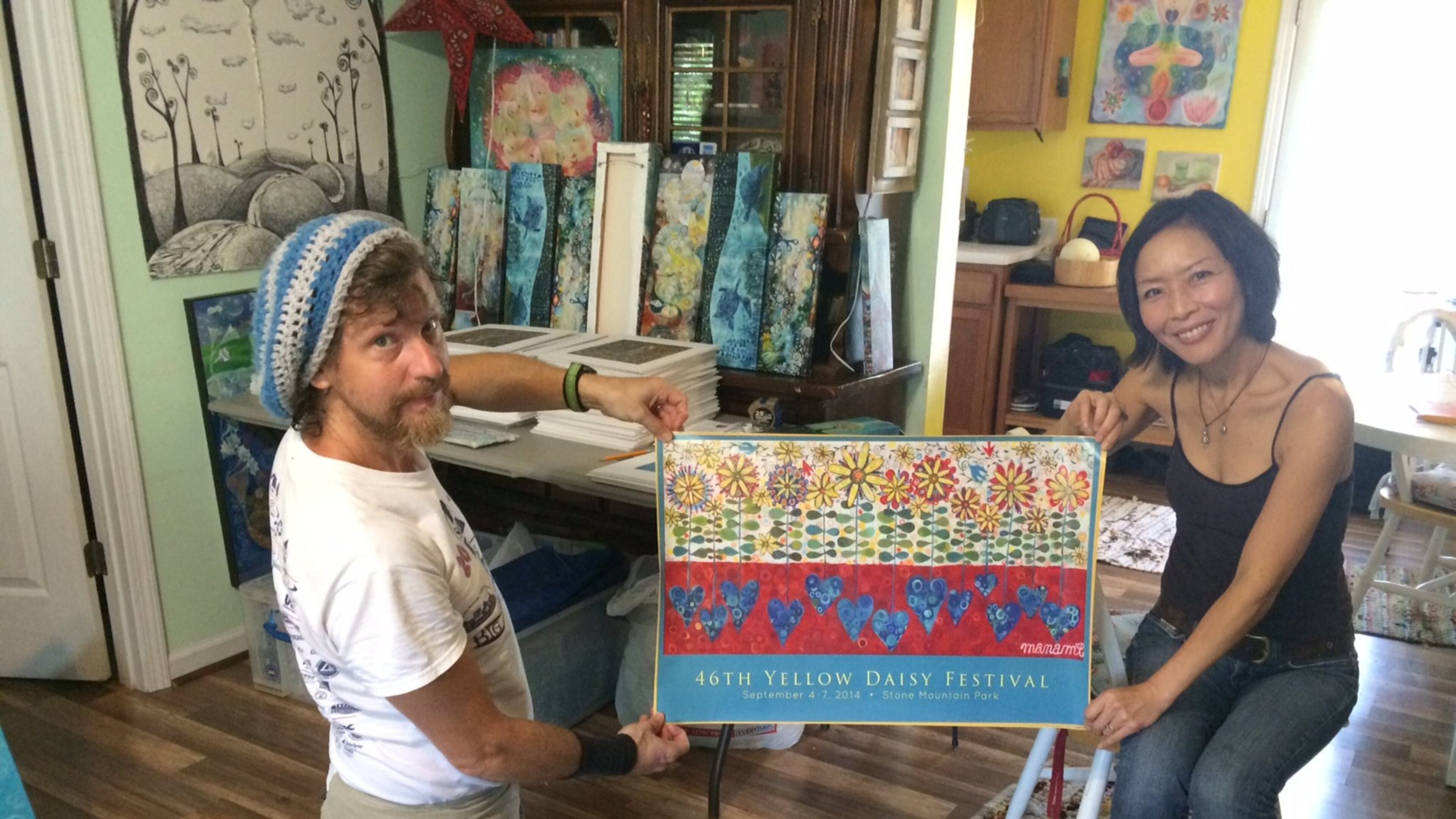 Manami Yagashiro Lingerfelt and her husband, Tommy, with a copy of the official poster for this year’s Yellow Daisy Festival. As the featured artist at this year’s 46th festival, Manami Lingerfelt’s painting appears on the poster. Tommy Lingerfelt mats and makes many of the frames for his wife’s work and also helps create the prints made from her original acrylic or oil paintings on canvas. JILL VEJNOSKA / JVEJNOSKA@AJC.COM