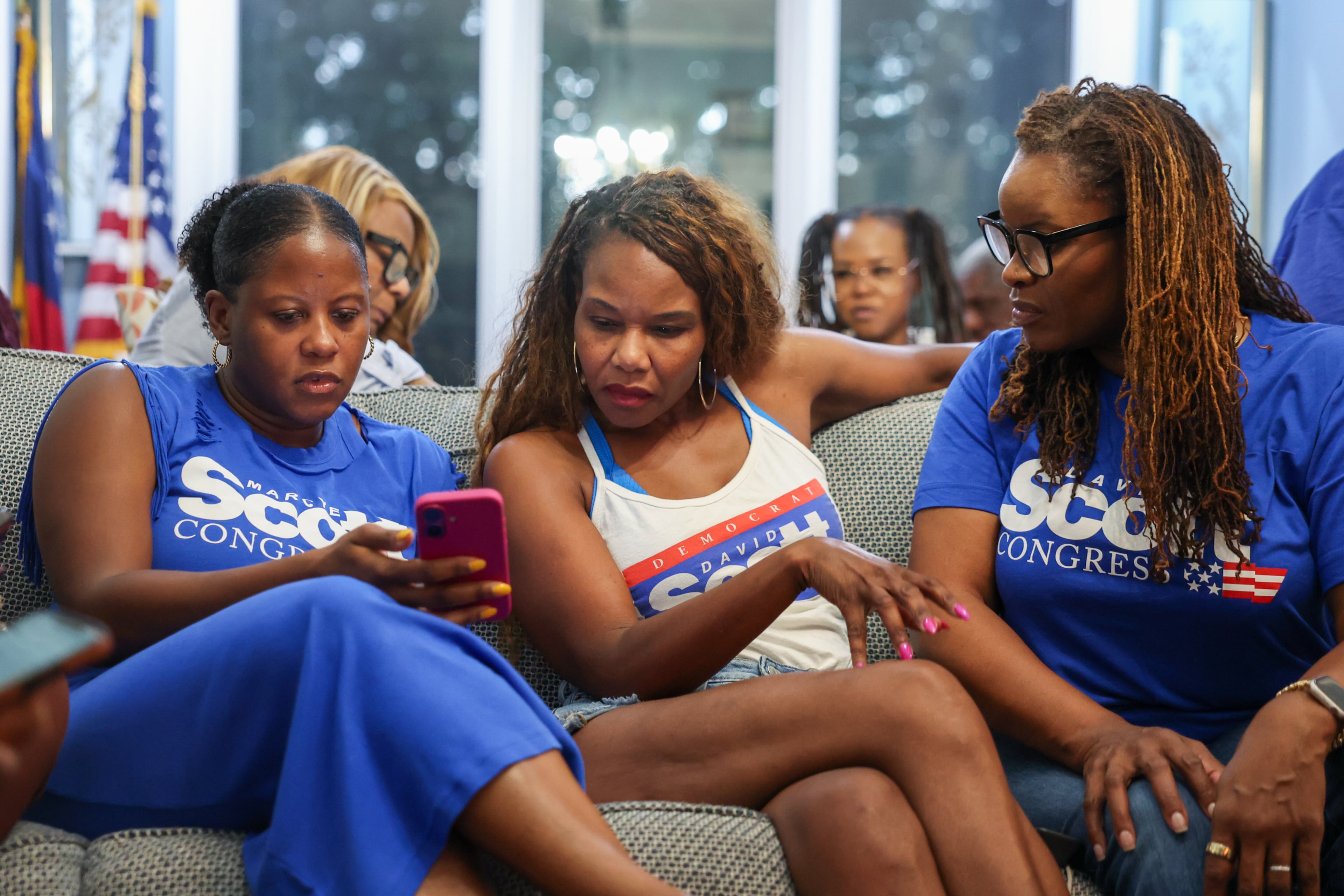 Democrat Marcye Scott (center), daughter of late Congressman David Scott and competing to complete her father’s term, looks at cousin Natasha Dale’s phone for the special runoff election returns during a watch party at her parents’ home in Atlanta on Aug. 25, 2026. (Arvin Temkar/AJC)