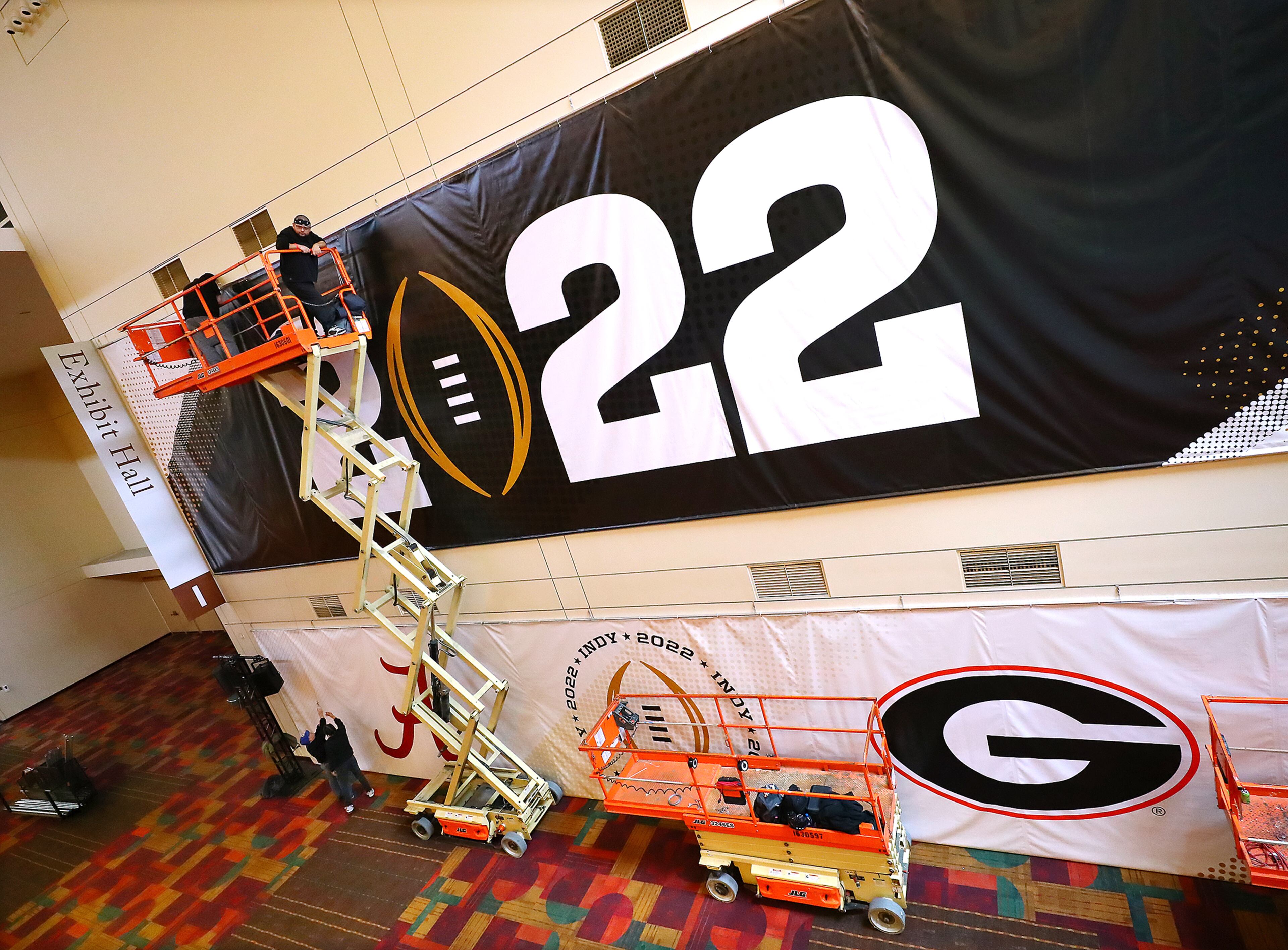 010622 Indianapolis: Workers hang a giant banner inside the Indianopolis Convention Center in preperation for fan fest events for the national championship game between Georgia and Alabama on Thursday, Jan. 6, 2022, in Indianapolis. “Curtis Compton / Curtis.Compton@ajc.com”`