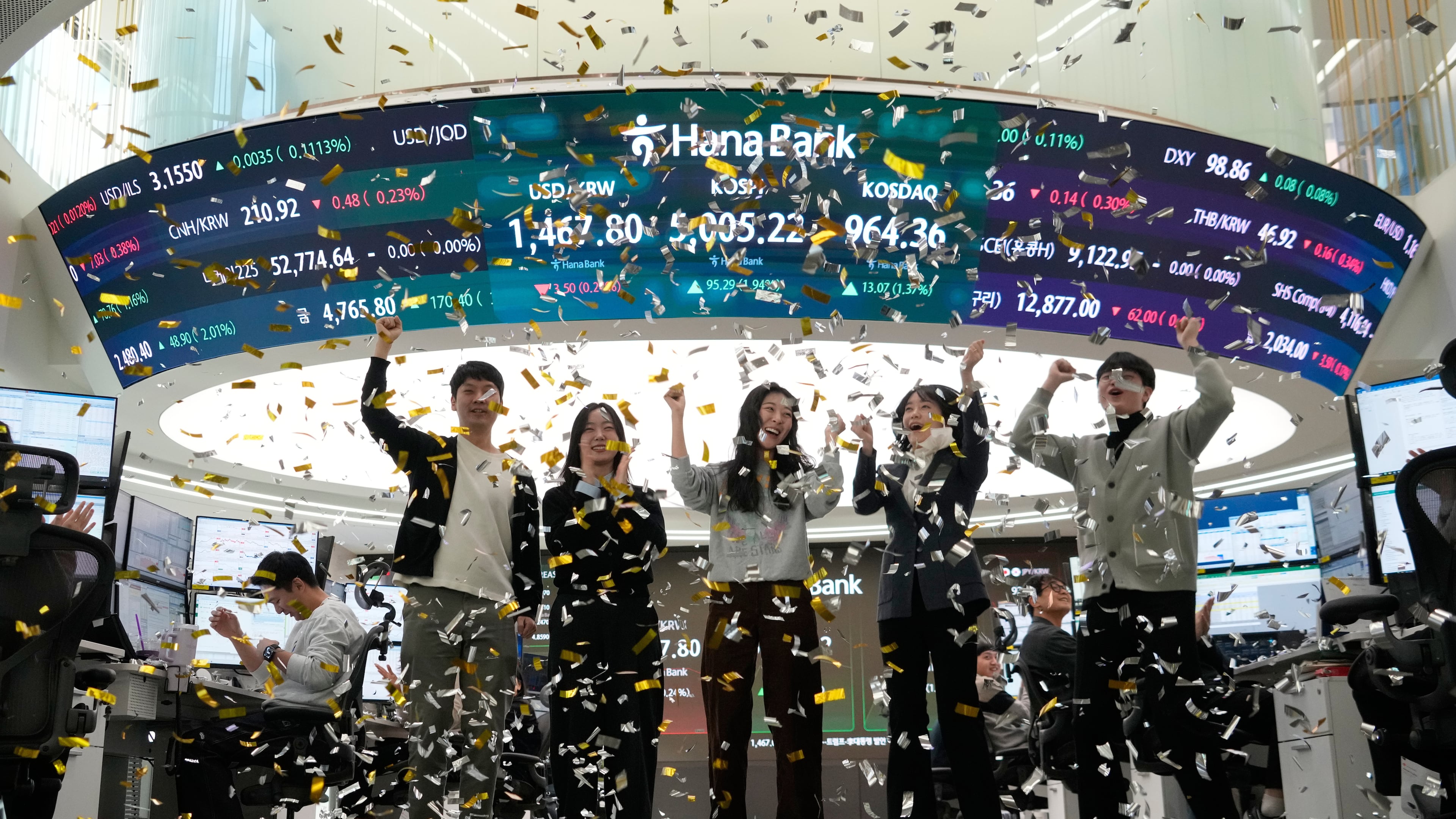 Currency traders celebrate as they work in the office with a screen showing the Korea Composite Stock Price Index (KOSPI), center top, of over 5,000 points at the foreign exchange dealing room of the Hana Bank headquarters in Seoul, South Korea, Thursday, Jan. 22, 2026. (AP Photo/Ahn Young-joon)