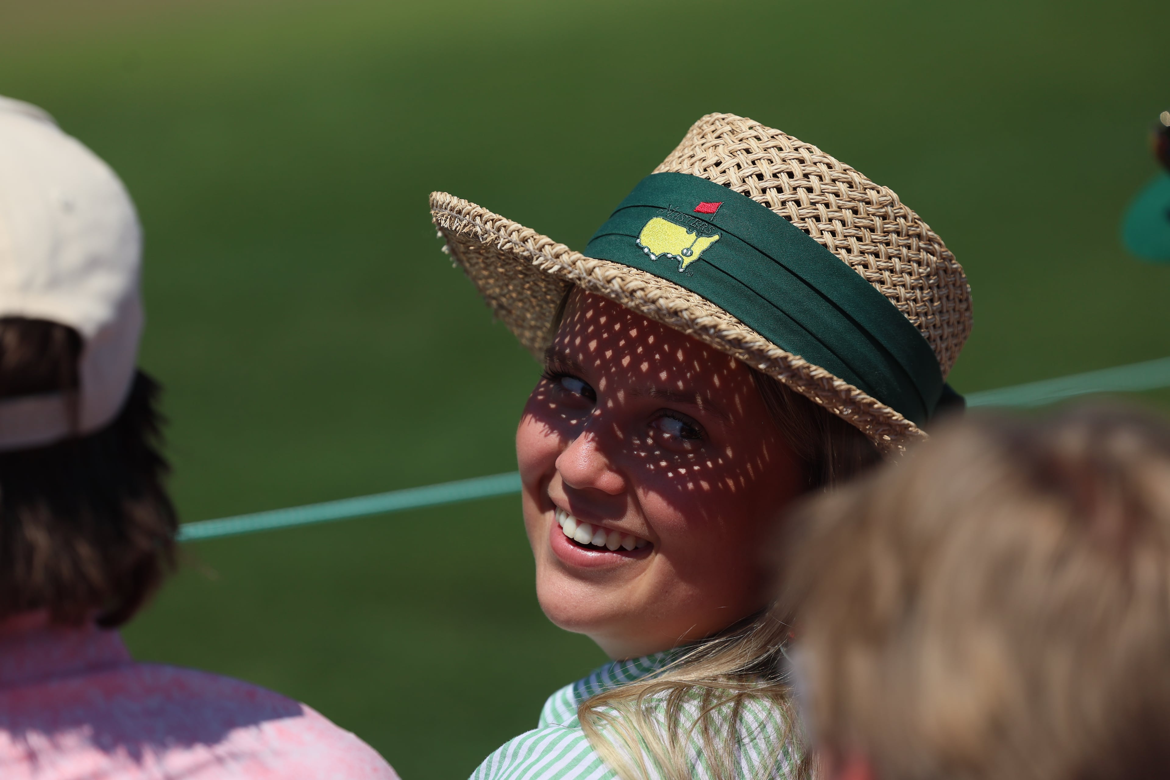 Patron in sunhat talks to person on second green during final round of the Masters, at Augusta National Golf Club, Sunday, April 12, 2026, in Augusta, GA (Jason Getz/AJC)
