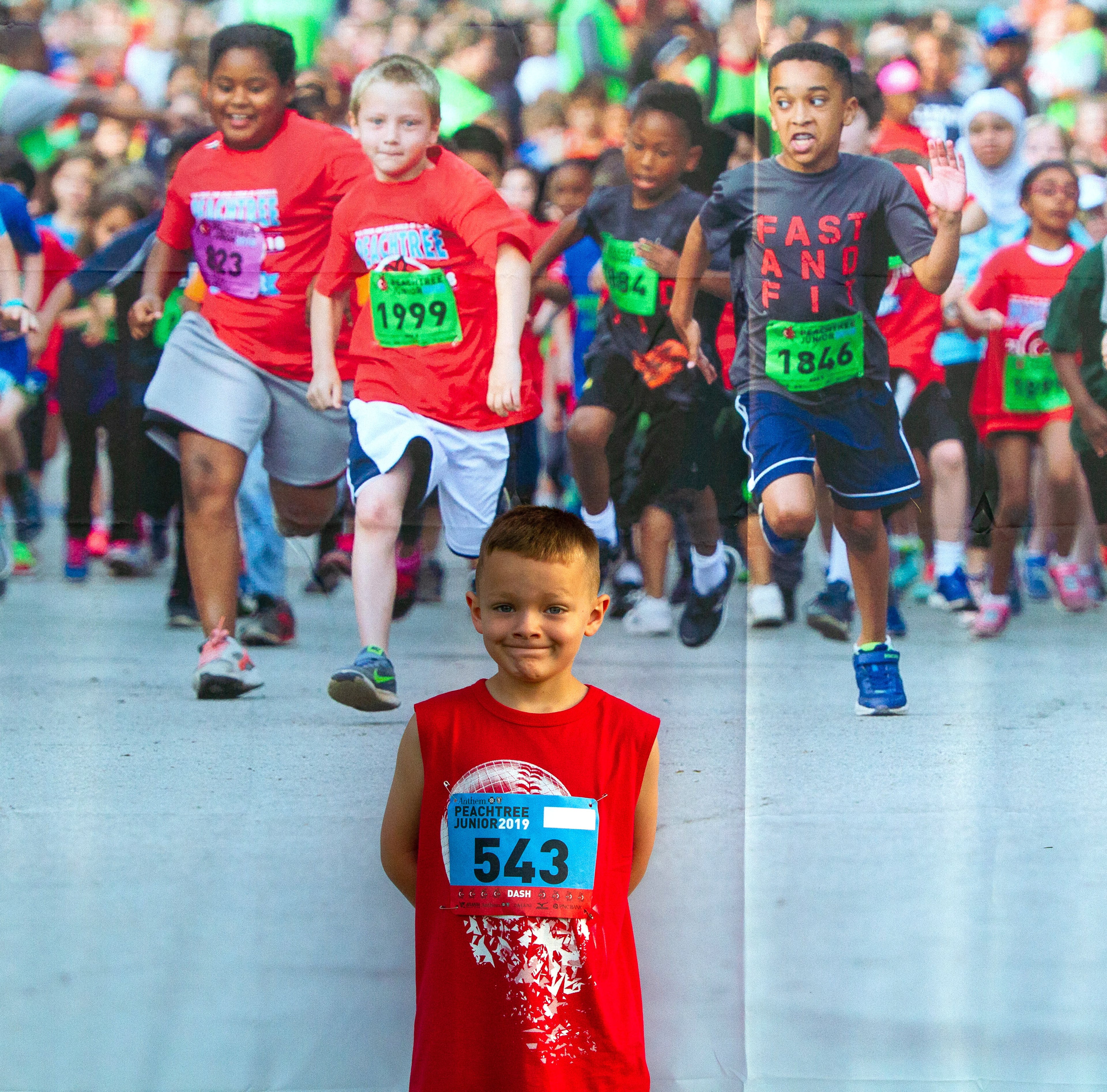 Hunter Williams poses for a photograph in front of a poster in the meadow in Piedmont Park before the start of The Anthem Peachtree Junior race Wednesday, July 3, 2019. The race included a Mile run; witch finished under the same finish line as the AJC Peachtree Road Race. STEVE SCHAEFER / SPECIAL TO THE AJC