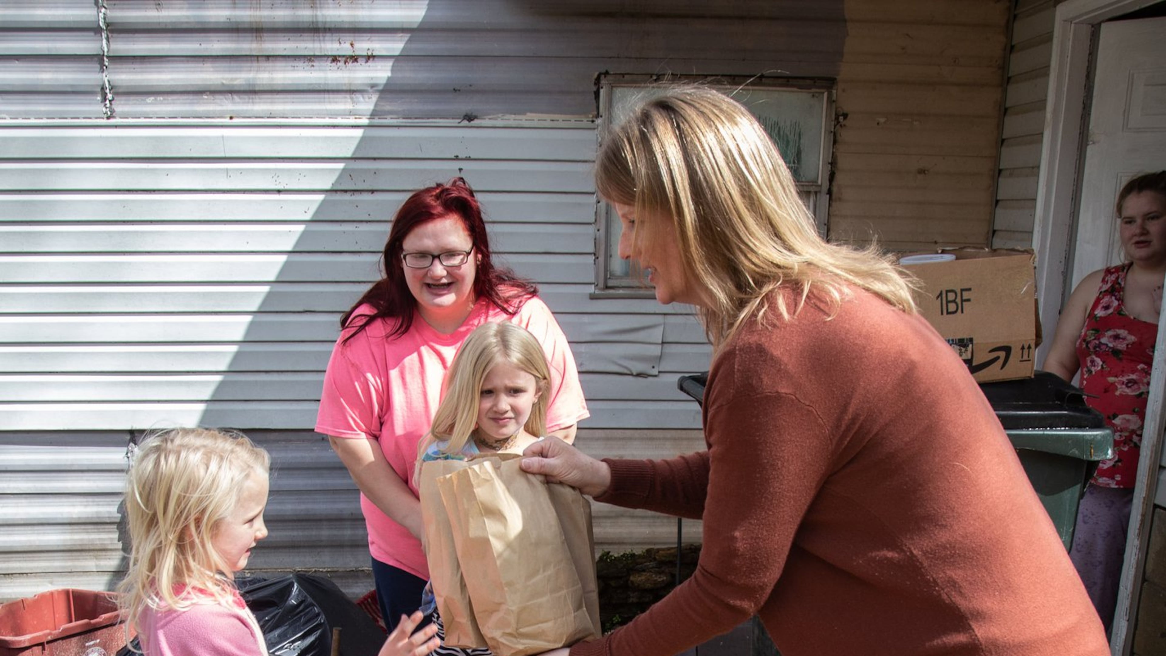 Marianne Glaser delivers lunches to Paisley Hugenschmidt as her mother, Katherine Hugenschmidt, and her sister Samantha look on Wednesday, March 25, 2020. STEVE SCHAEFER / SPECIAL TO THE AJC