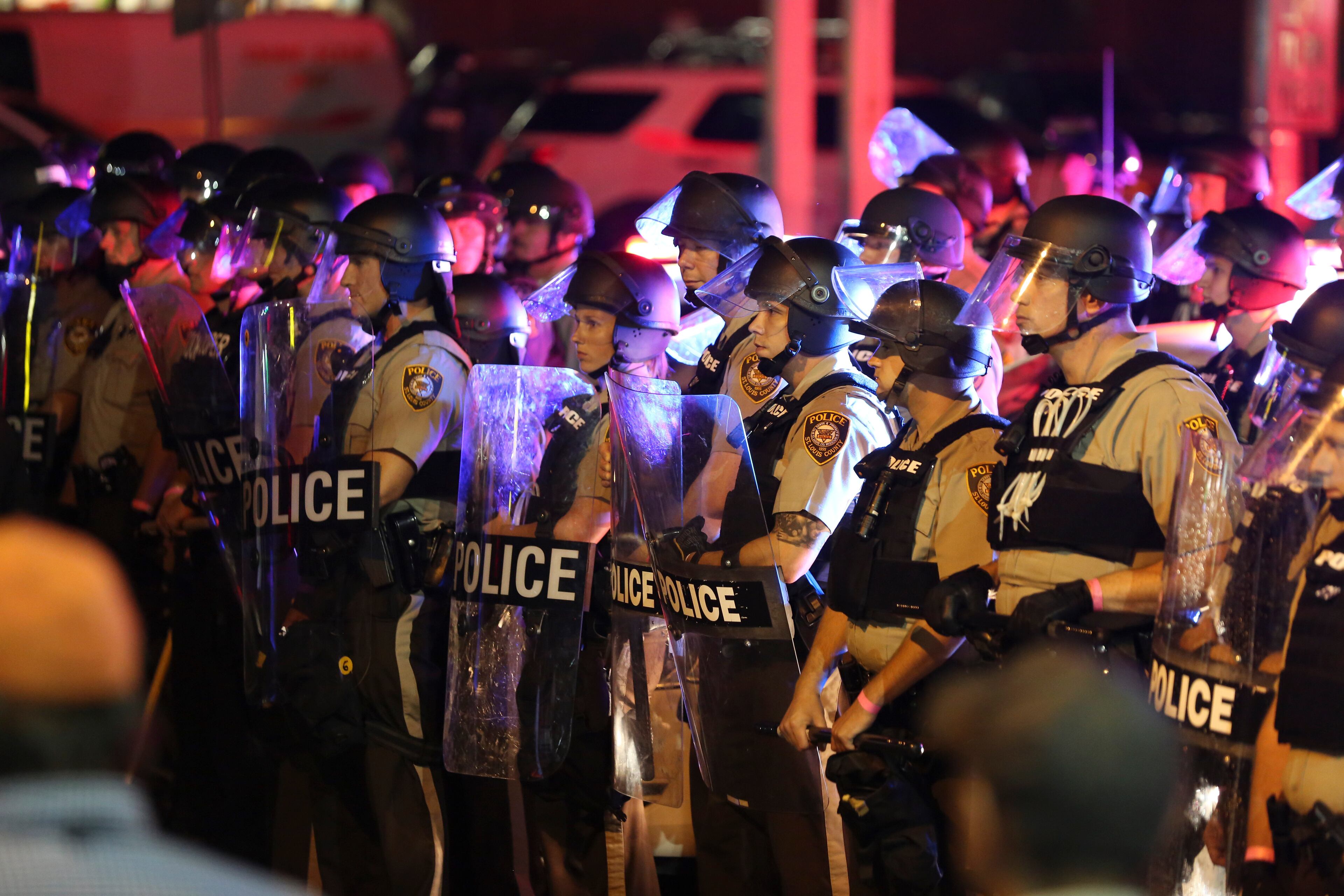 Police officers in riot gear gather on West Florissant Avenue as protesters march on the anniversary of the fatal shooting of Michael Brown by a police officer in Ferguson, Mo., Aug. 9, 2015. A day of peaceful protest commemorating the killing of an unarmed black teenager by a white police officer one year ago ended in gunfire later Sunday. A St. Louis County police officer was involved in the shooting, the department said. (Whitney Curtis/The New York Times)
