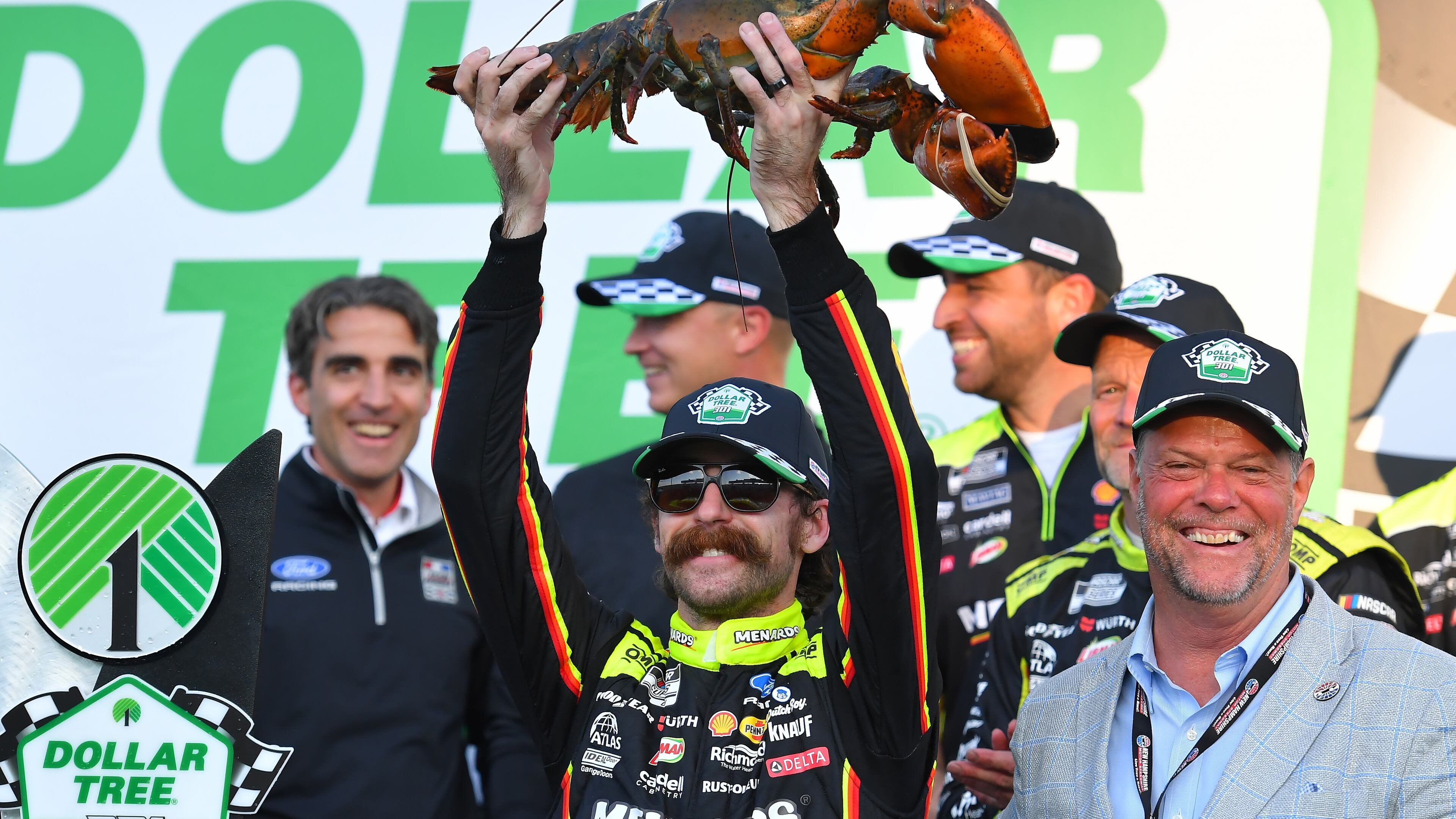 Ryan Blaney, center front, displays a lobster, a Victory Lane tradition at New Hampshire Motor Speedway, after winning a NASCAR Cup Series auto race, Sunday, Aug. 23, 2026, at the speedway in Loudon, N.H., as David McGrath, right, executive vice president and general manager of the speedway looks on. (AP Photo/Steven Senne)