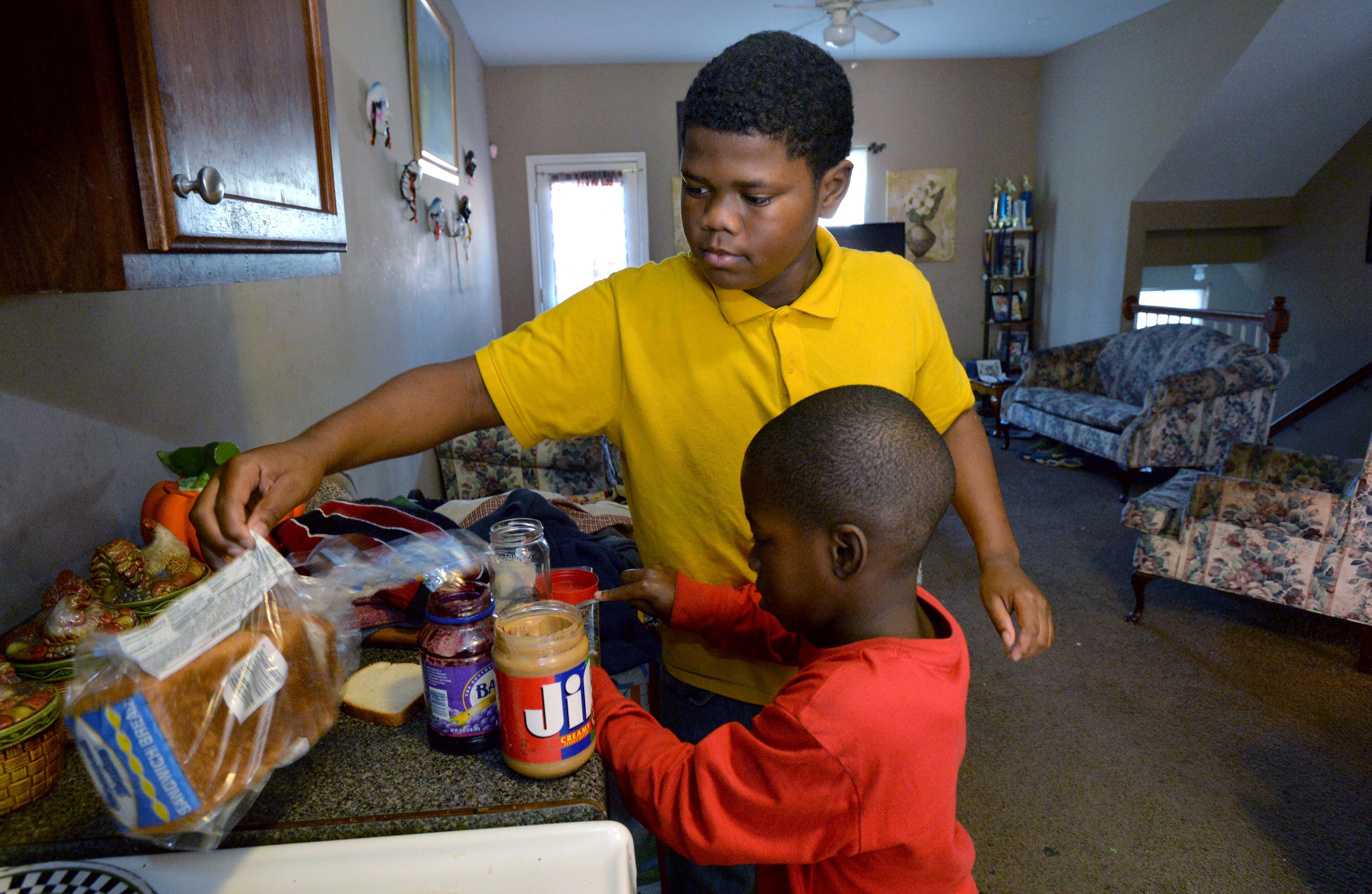Dazmine Marshall, 18, and Damyuss, 8, make peanut butter and jelly sandwiches for their breakfast. HYOSUB SHIN / HSHIN@AJC.COM