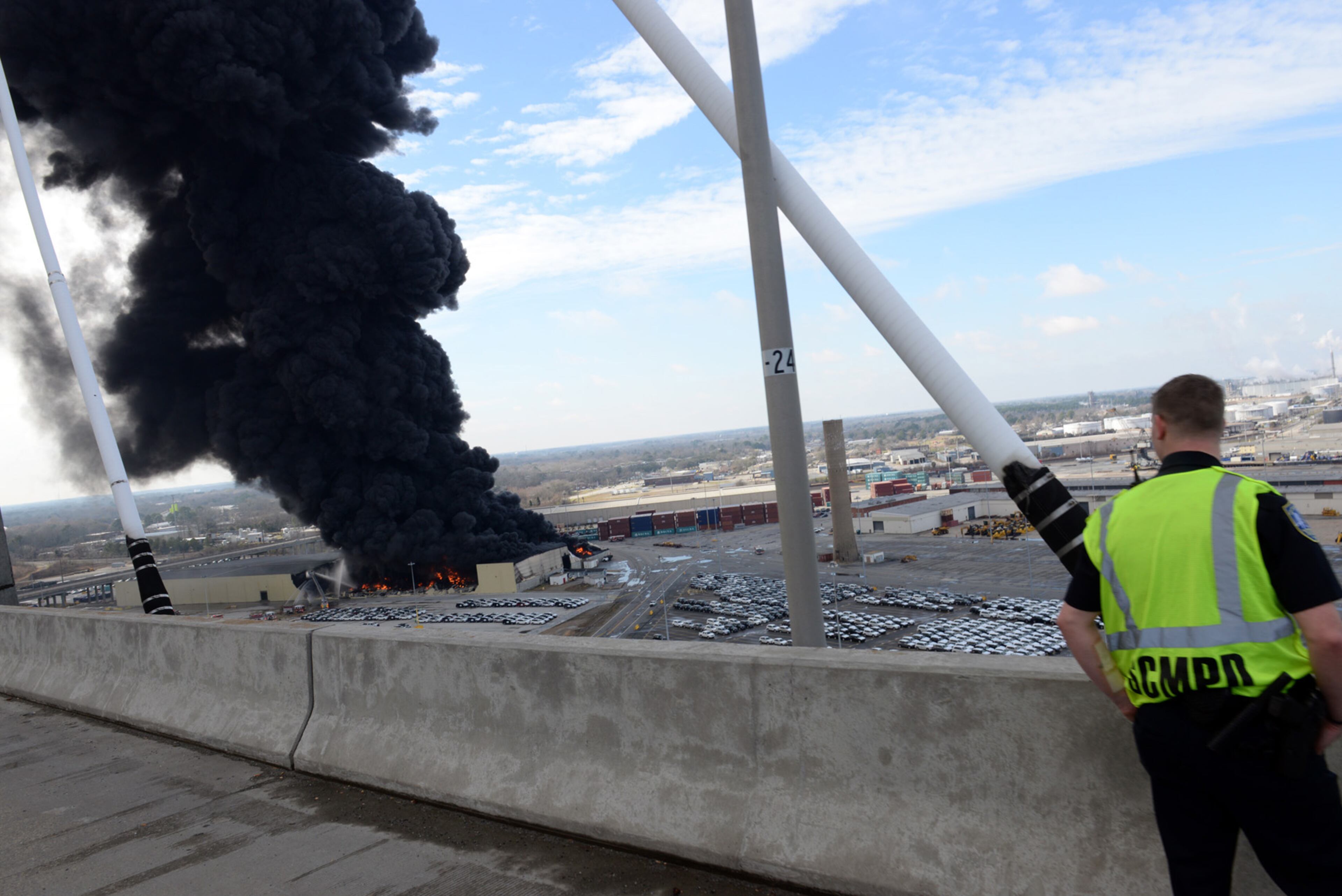 A Savannah-Chatham Metro Police officer watches from the Talmadge Bridge as smoke and flames pour from Ocean Terminal Warehouse No.3 at the Georgia Ports Authority on Saturday, Feb. 8, 2014. Burning rubber from the fire at the Port of Savannah sent up a towering column of black smoke that could be seen from miles away. The cause of the fire wasn't immediately known, but all port workers were accounted for and unharmed.(AP Photo/Savannah Morning News, Richard Burkhart)