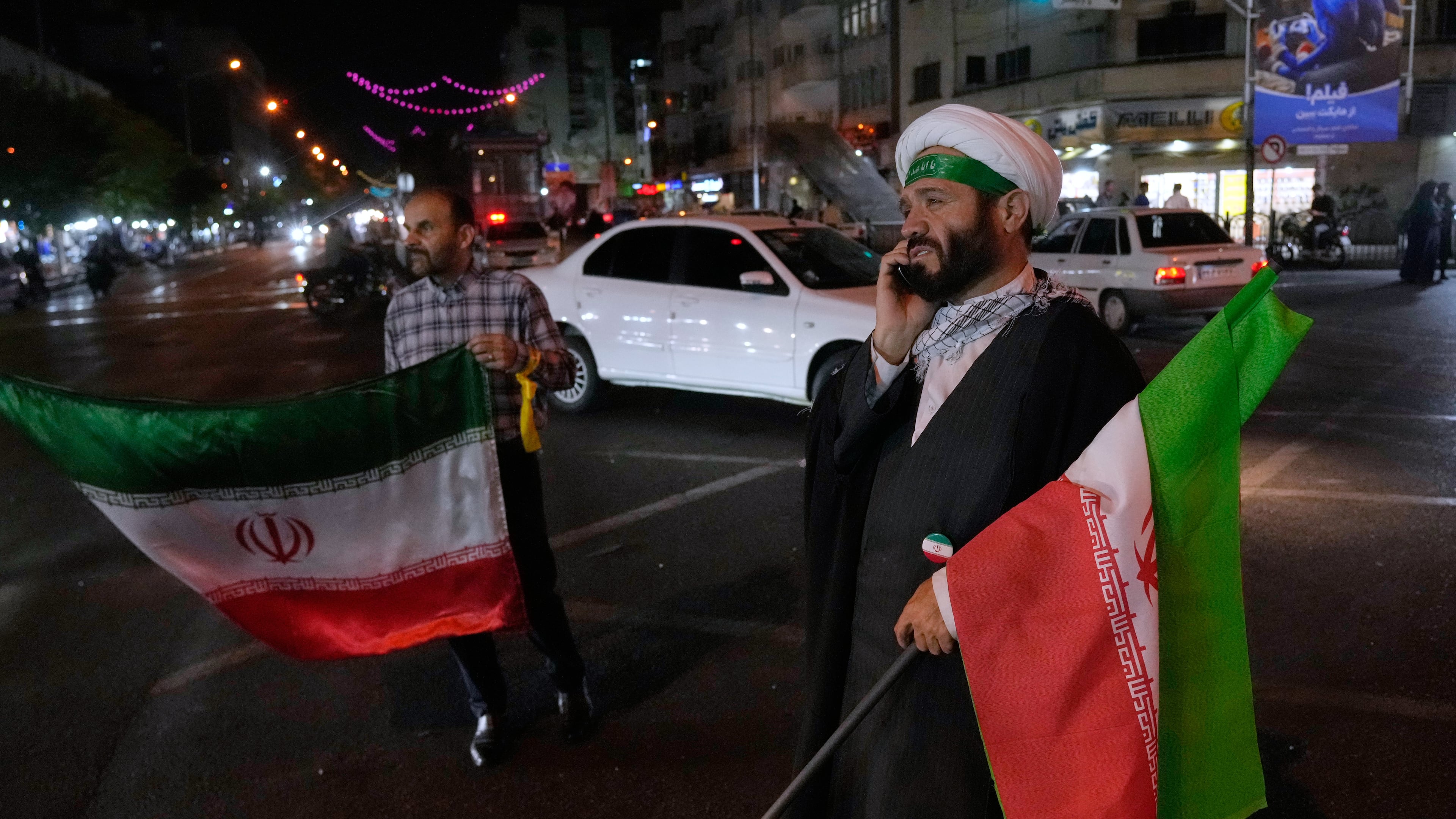 A cleric speaks on his cellphone holding an Iranian flags for a pro-government campaign in downtown Tehran, Iran, Friday, May 8, 2026. (AP Photo/Vahid Salemi)