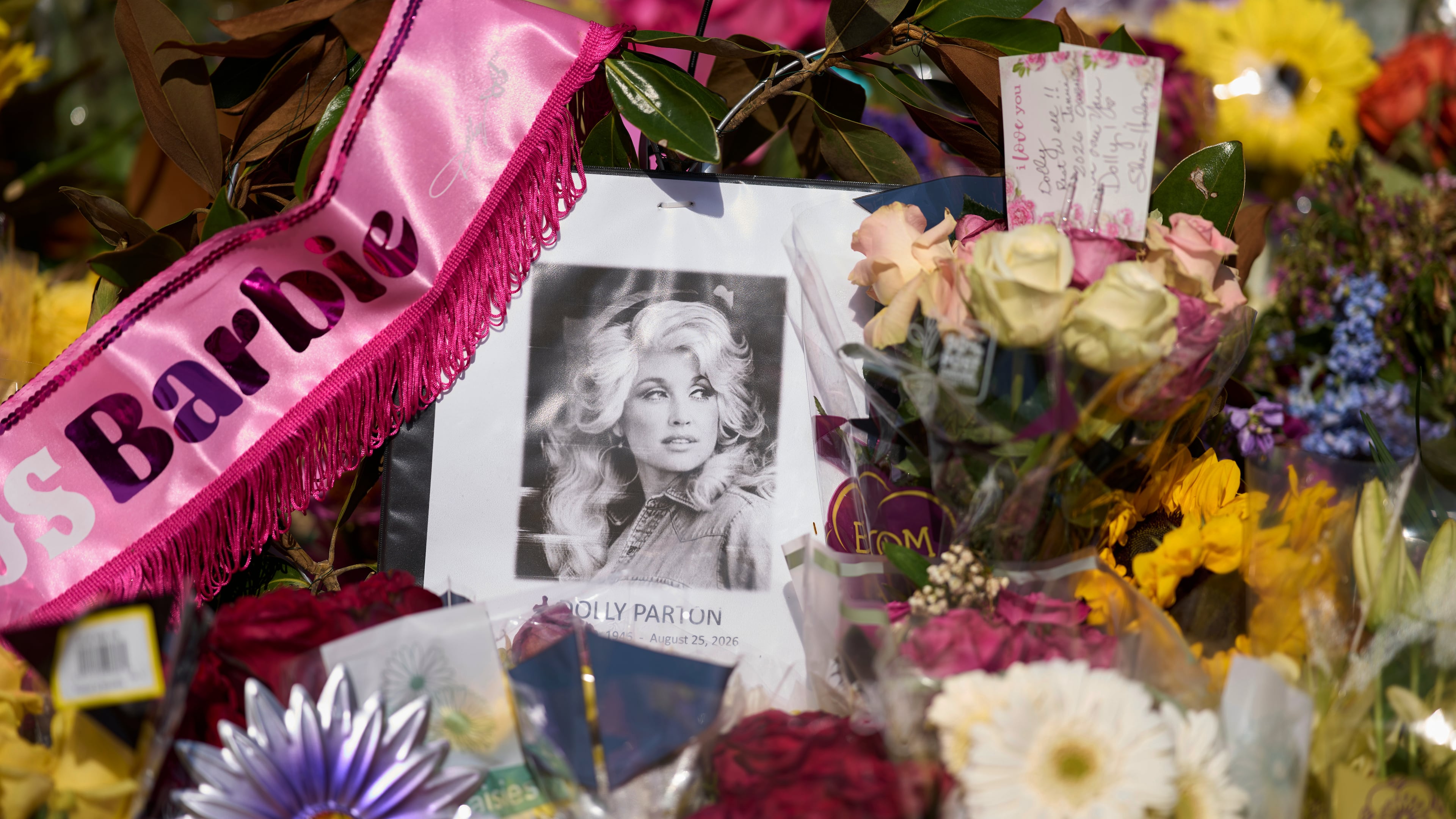 A portrait of the late Dolly Parton surrounded by flowers and cards in a memorial sits outside her home Thursday, Aug. 27, 2026, in Brentwood, Tenn. (AP Photo/George Walker IV)