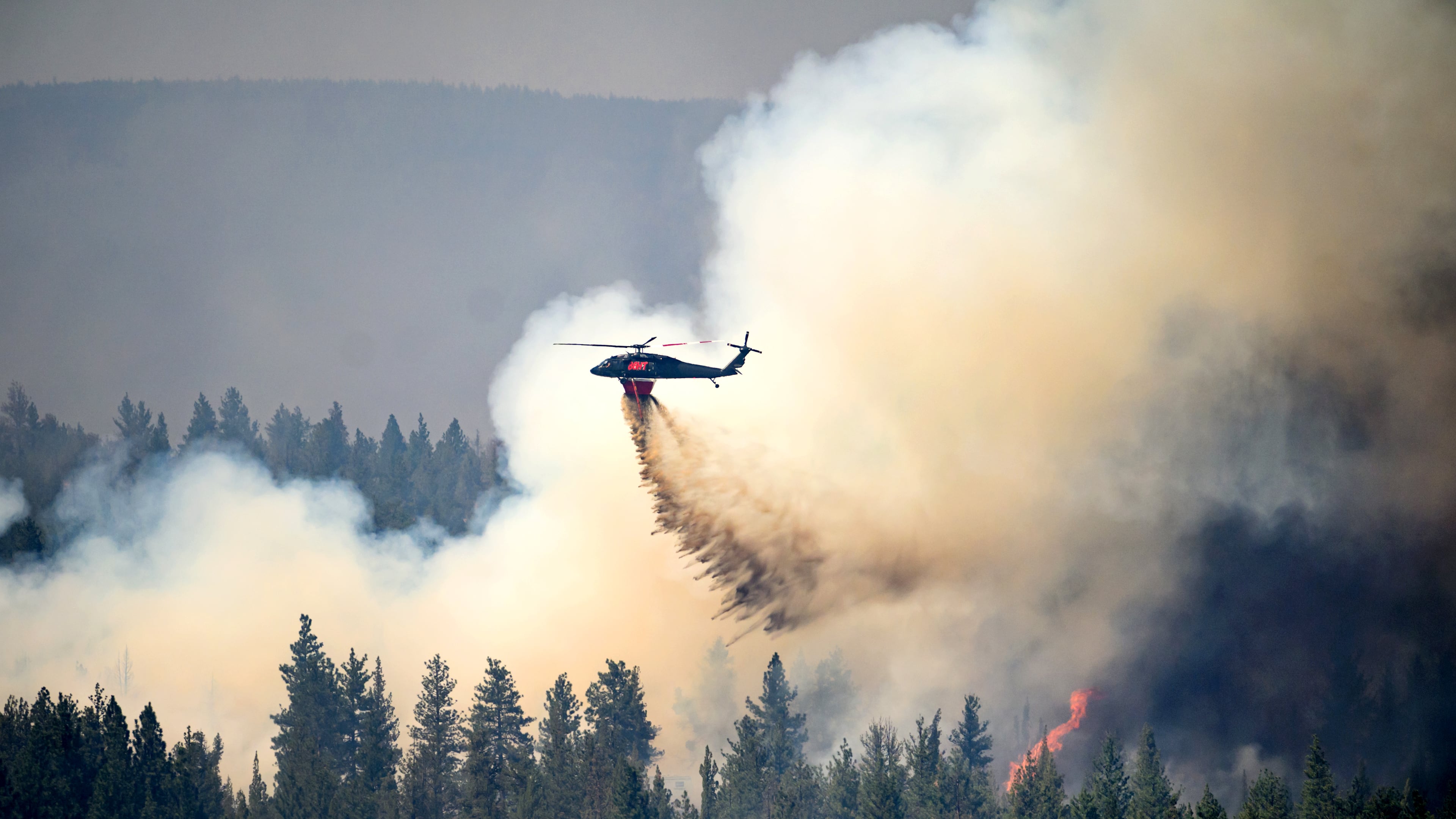 A helicopter drops water on the Akawa Butte fire on Friday, July 24, 2026, near Sisters, Ore. (AP Photo/Noah Berger)