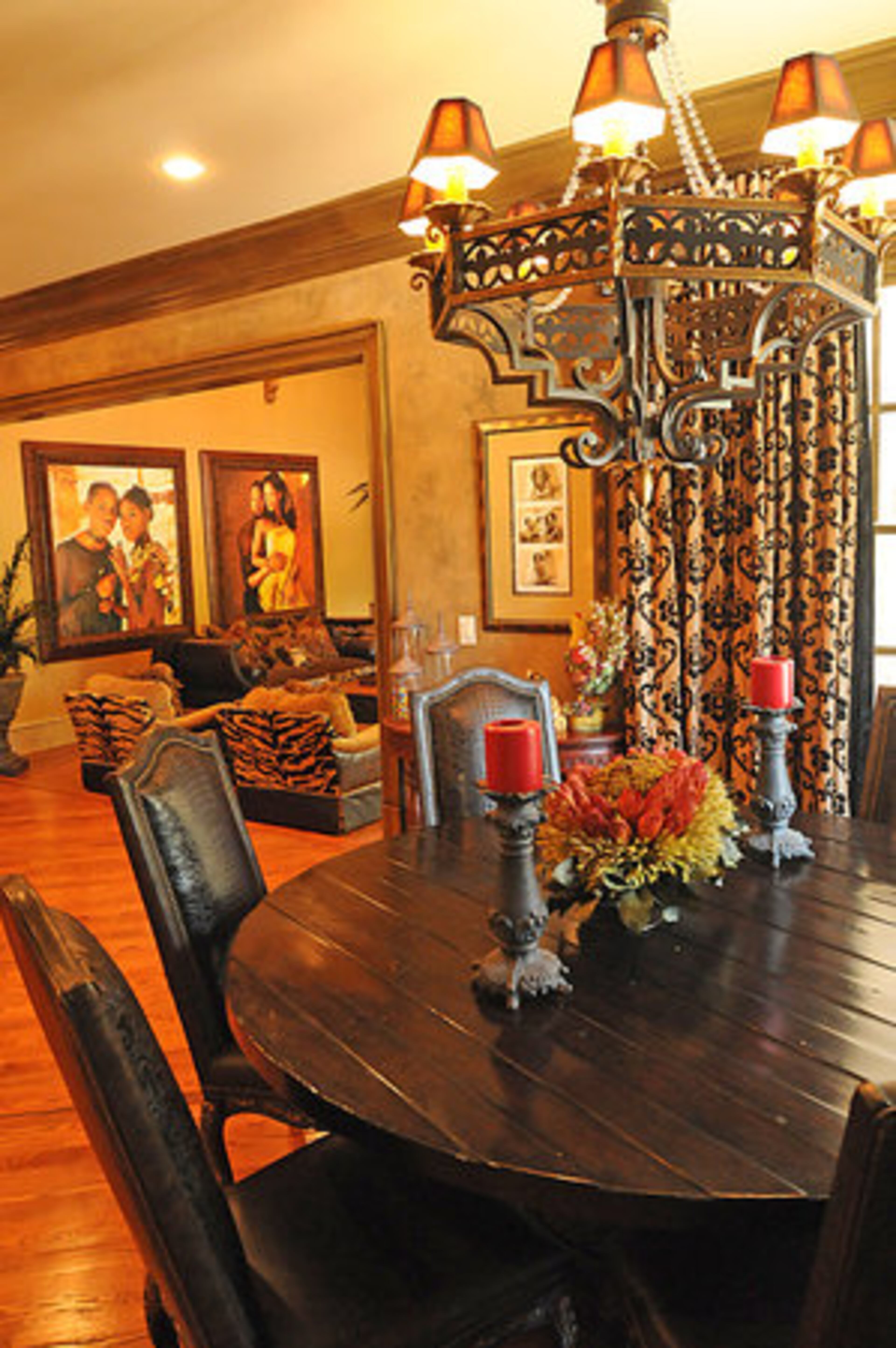 The formal dining room features a round table made of rich, dark wood and handsome, richly upholstered chairs. The table is lit by an ornate light fixture, one of several located throughout the home.