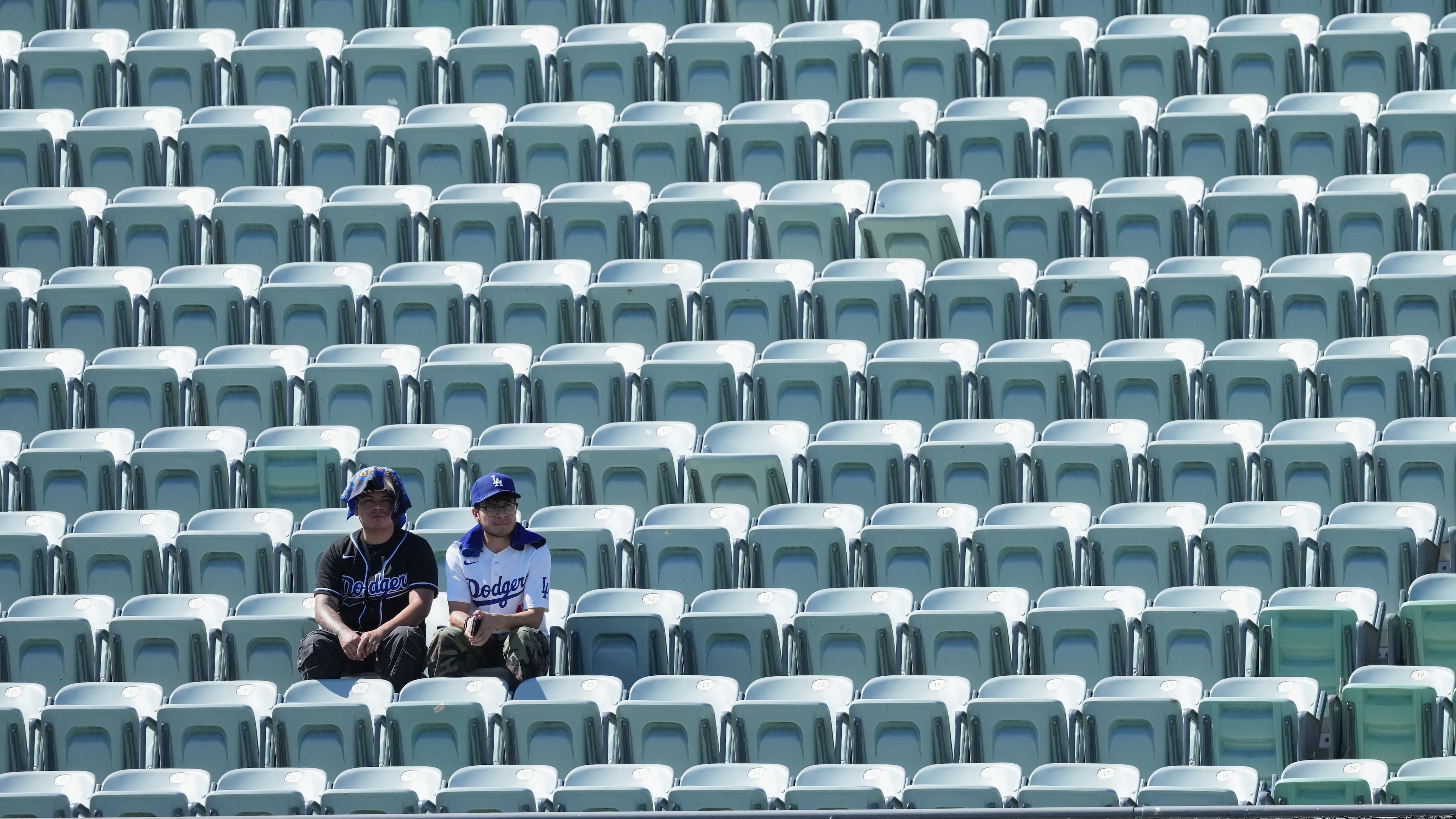 Los Angeles Dodgers fans look on among empty seats as they shield themselves from the sun and heat before Game 1 of a National League Division Series baseball game against the Atlanta Braves Saturday, Oct. 3, 2026, in Los Angeles. (AP Photo/Jae C. Hong)