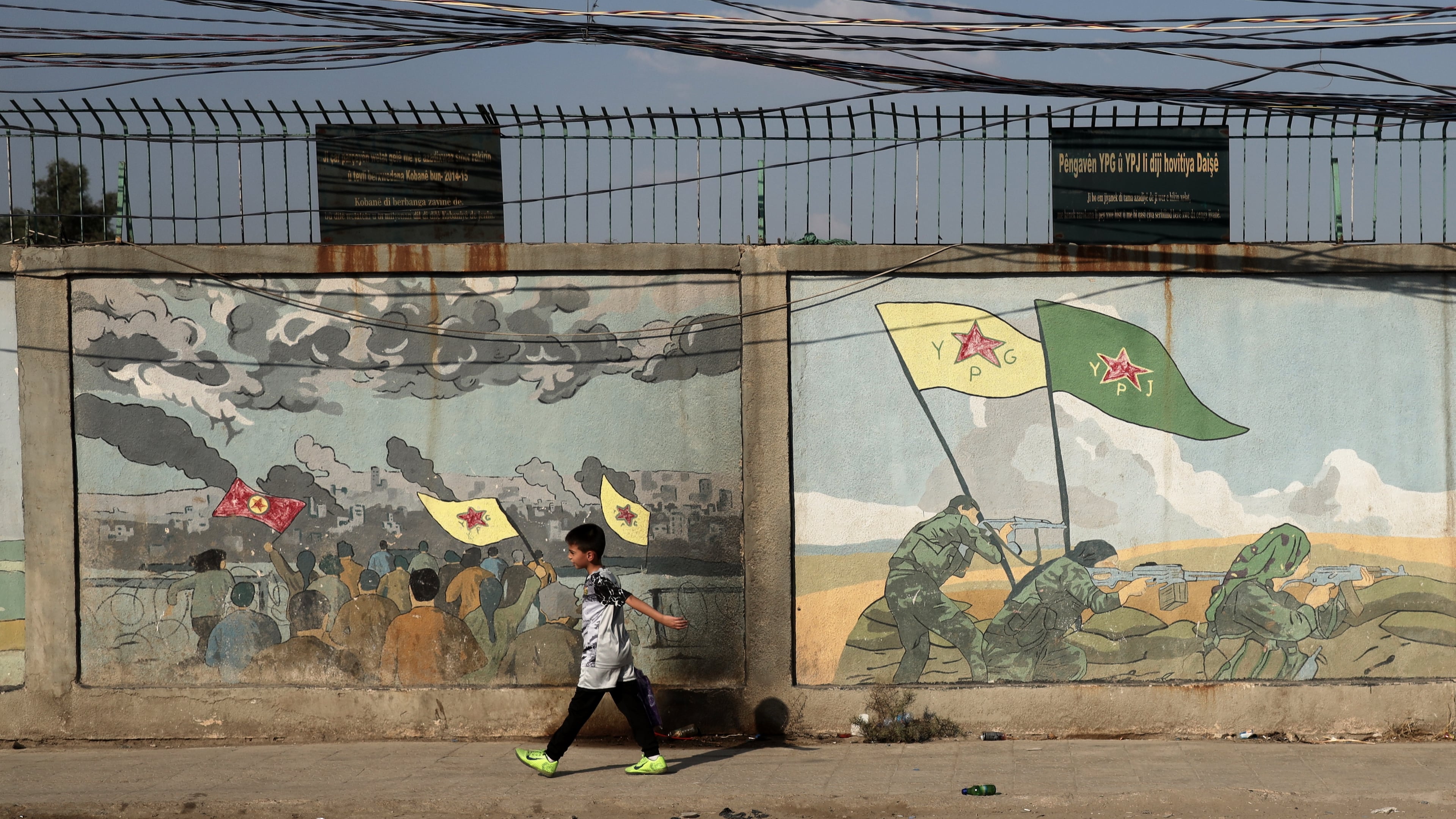 A boy walks past murals depicting Kurdish YPG and YPJ fighters battling Islamic State militants in Qamishli, northeastern Syria, Wednesday, Aug. 26, 2026. (AP Photo/Baderkhan Ahmad)