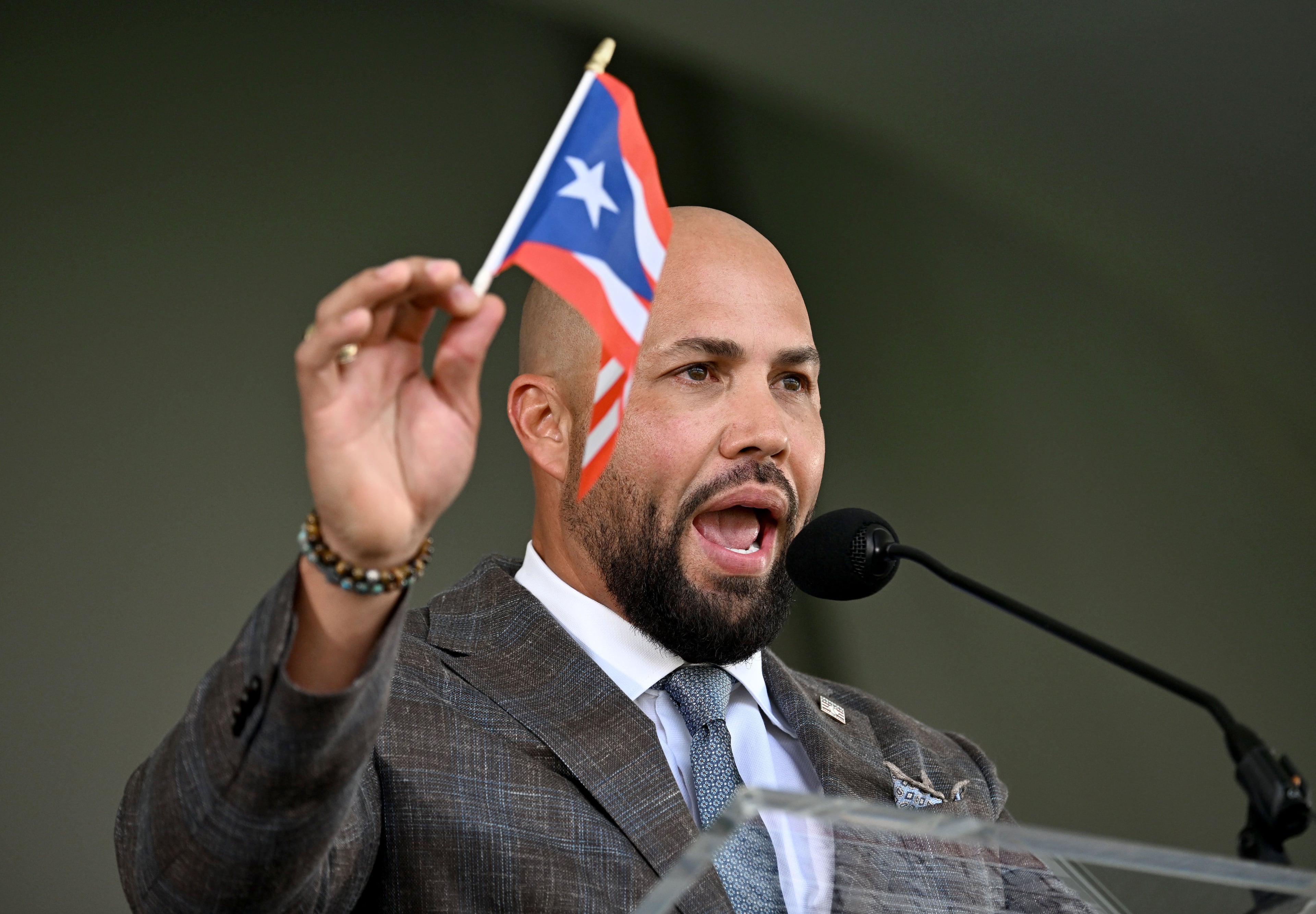 Carlos Beltrán speaks while holding a Puerto Rico flag during the 2026 National Baseball Hall of Fame Induction Ceremony at the Clark Sports Center on Sunday, July 26, 2026, in Cooperstown, N.Y. Braves centerfielder Andruw Jones is set for induction into the National Baseball Hall of Fame as part of the Class of 2026, alongside Carlos Beltrán and Jeff Kent. (Hyosub Shin/AJC)